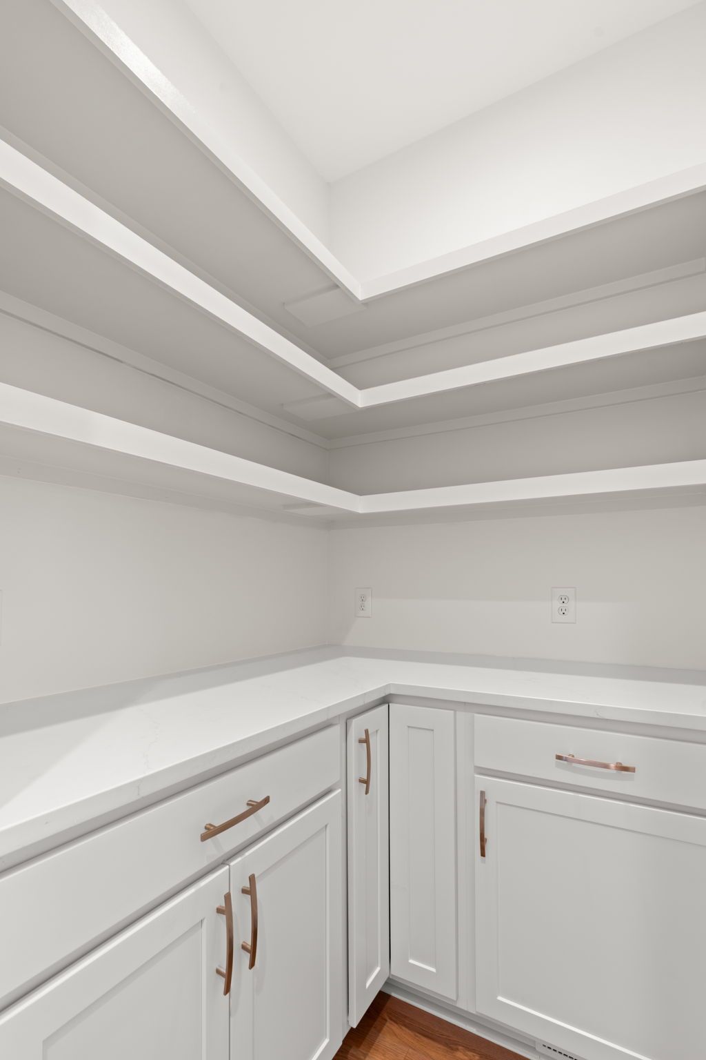 White built-in corner cabinets and countertop in a bright, empty room with stepped tray ceiling detail