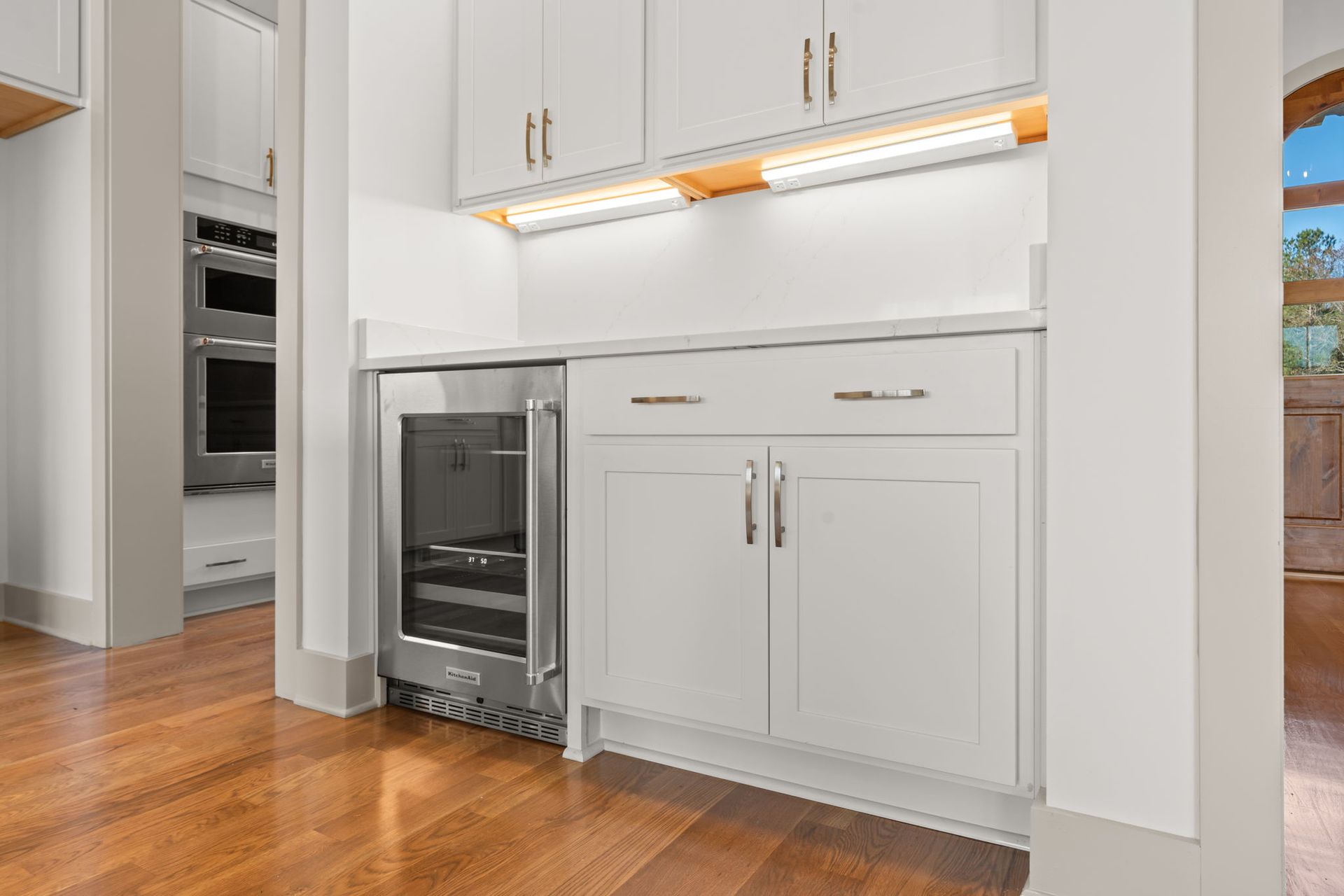 Modern kitchen with white cabinets, built-in oven, and wood floors; dishwasher open below the counter.