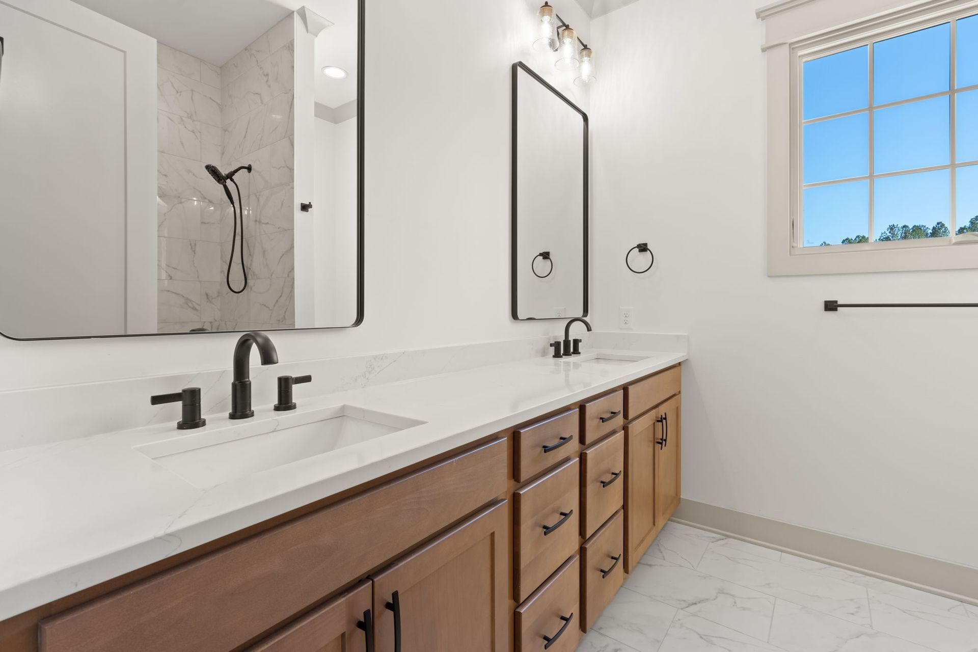 Bright bathroom with double vanity, large mirror, white counters, wood cabinets, and a window.