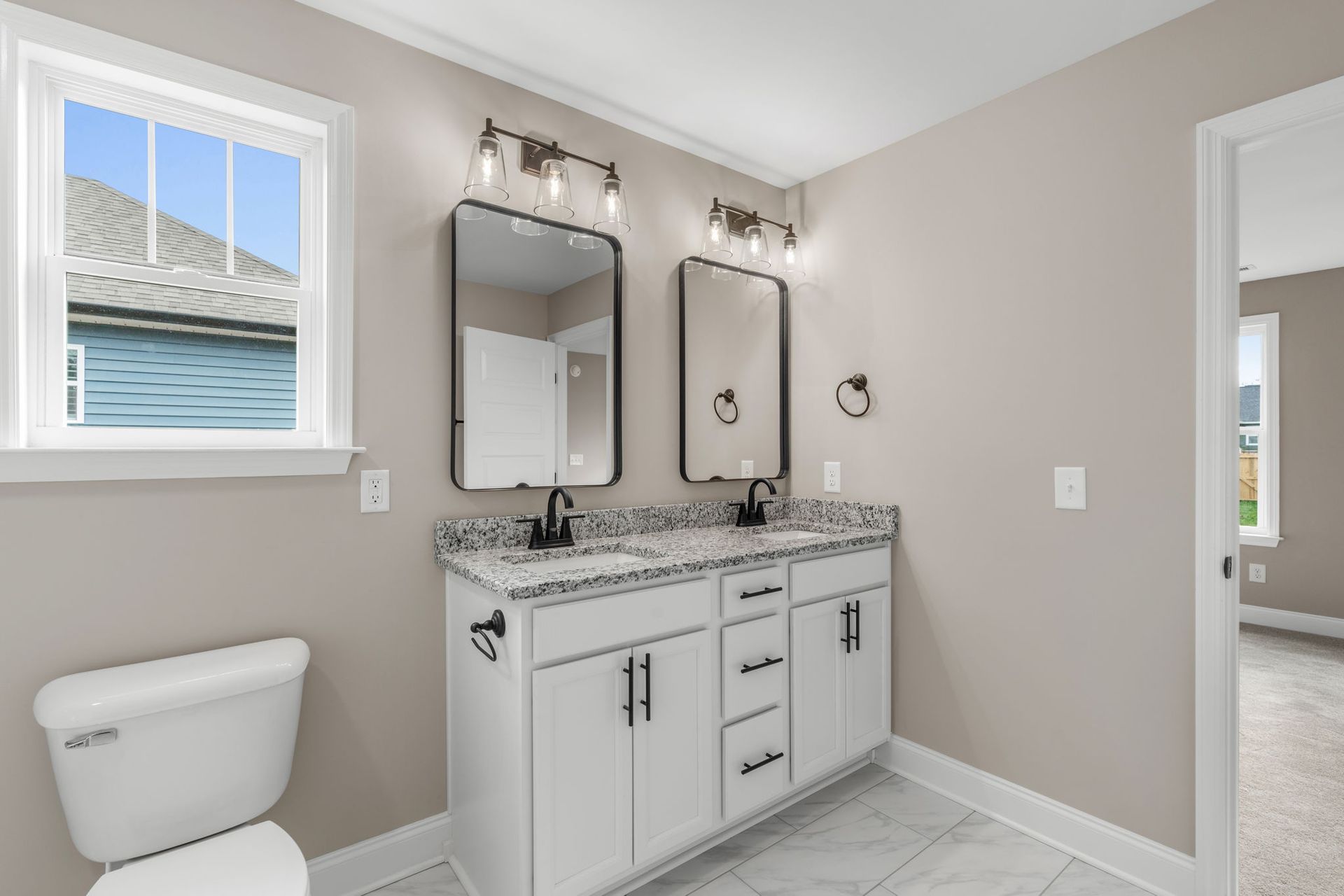 A bathroom with two sinks , two mirrors , a toilet and a window.