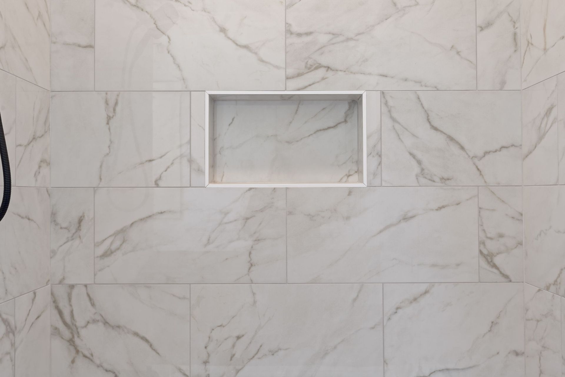 White marble-tile wall with a small rectangular recessed niche in the center.