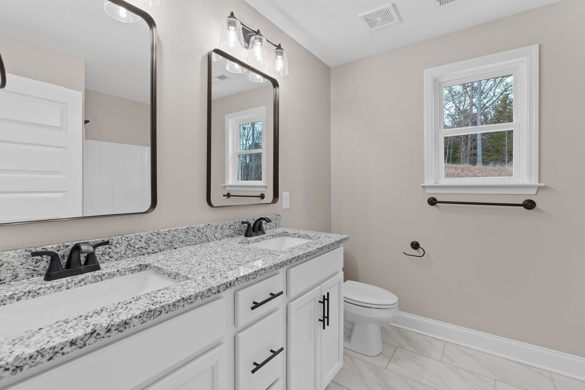 A bathroom with two sinks , two mirrors , a toilet and a window.
