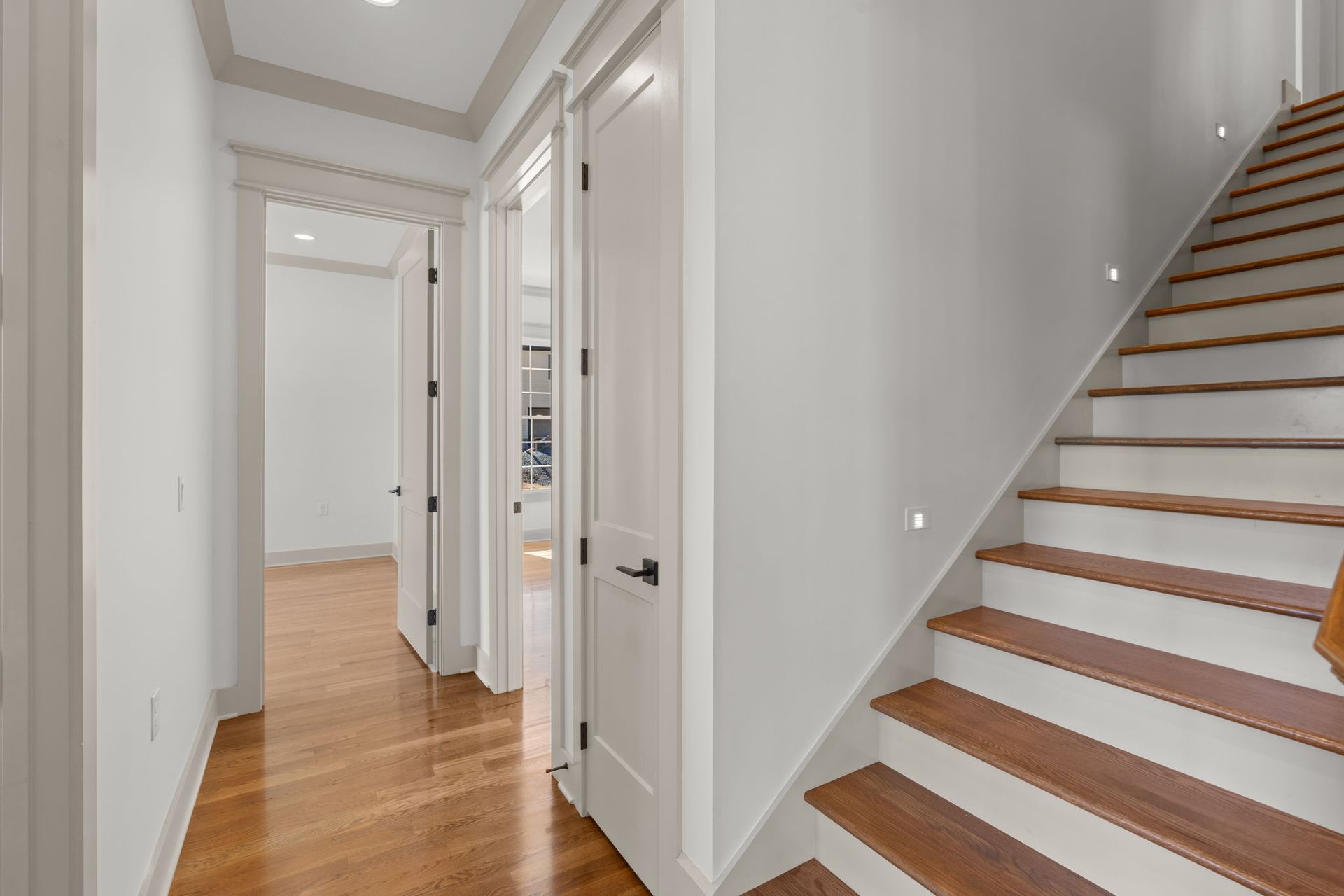 Bright hallway with hardwood floors, white walls, and a staircase on the right.