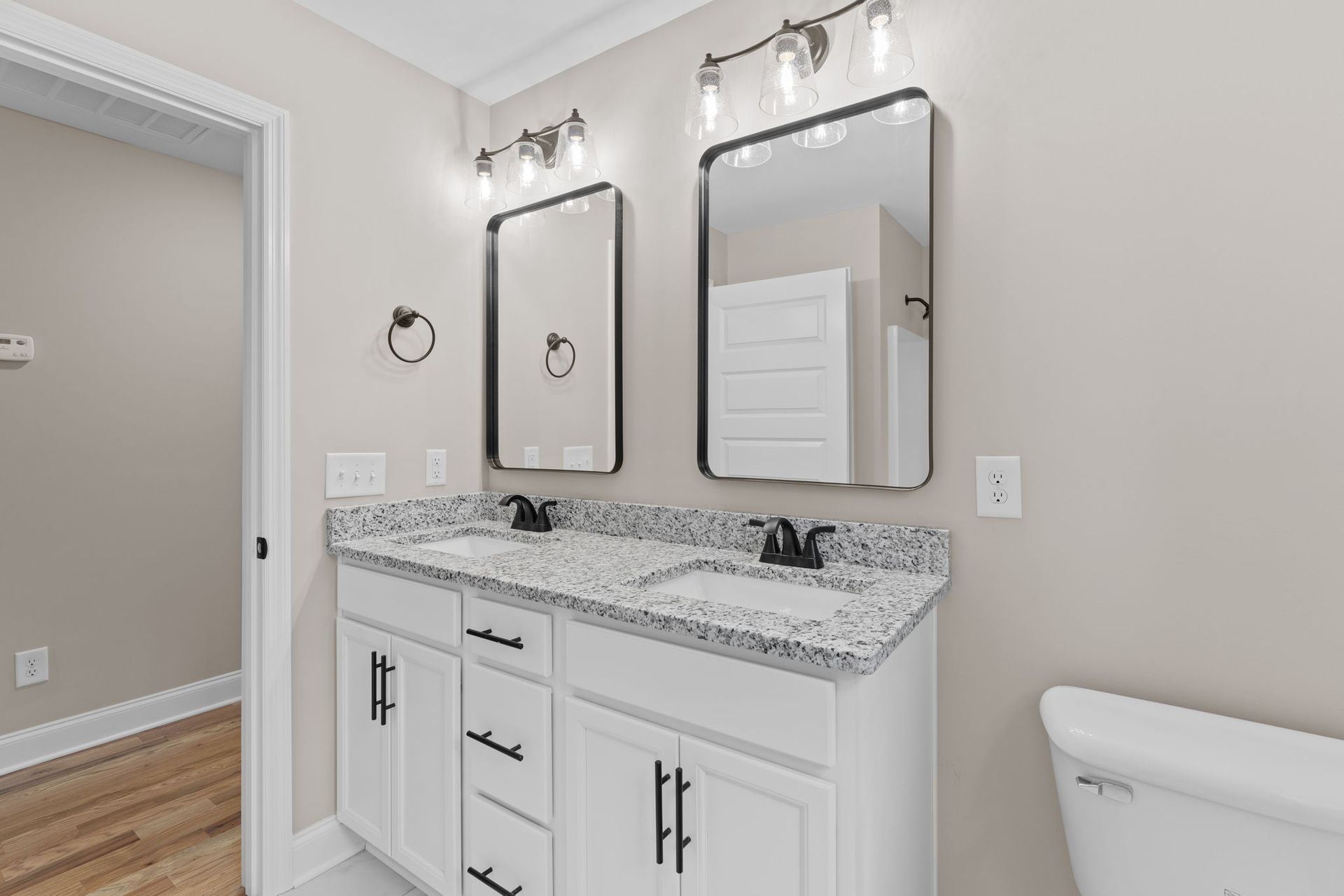 A bathroom with two sinks , two mirrors and a toilet.