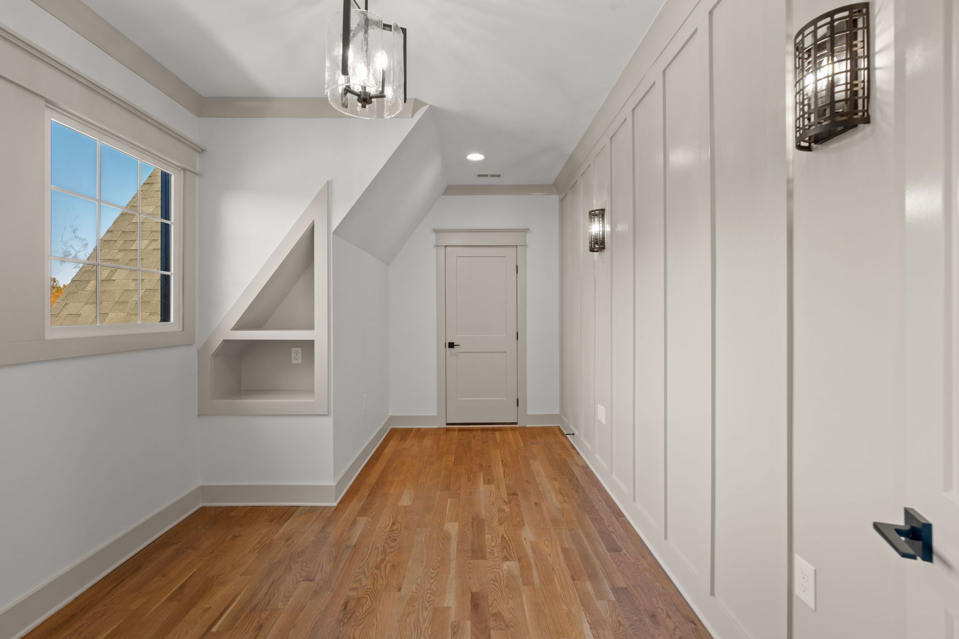 Bright hallway with wood floor, white walls, doors, window, and built-in shelving.