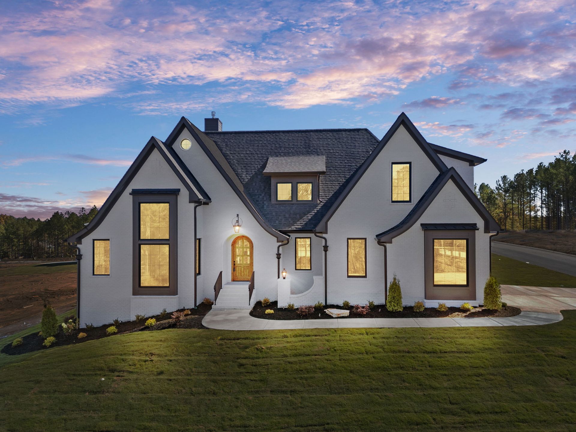 Modern white house with dark roof and lit windows at dusk under a pastel sky