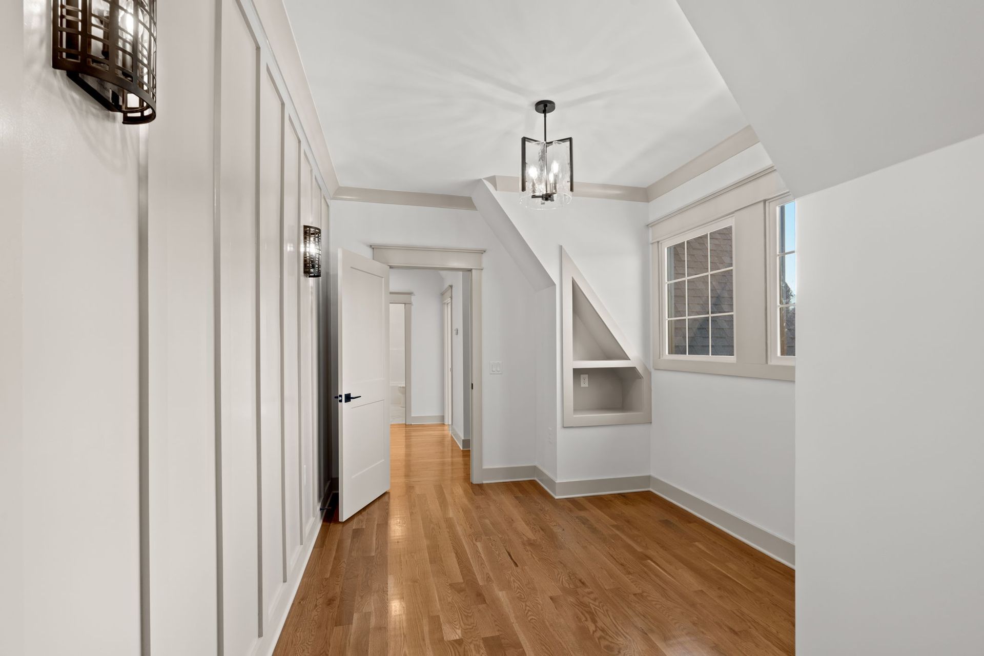 Bright hallway with white walls, wood floor, windows, and a hanging light fixture.