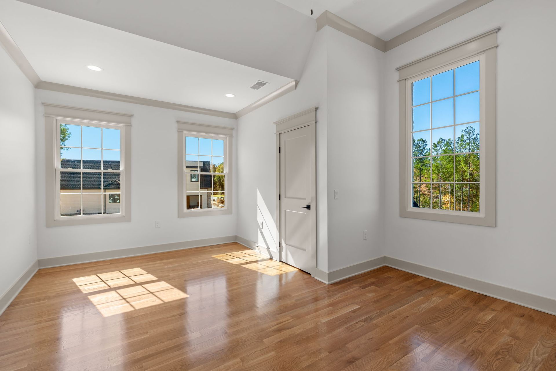 Bright empty room with hardwood floors, white walls, and sunlight from multiple windows.