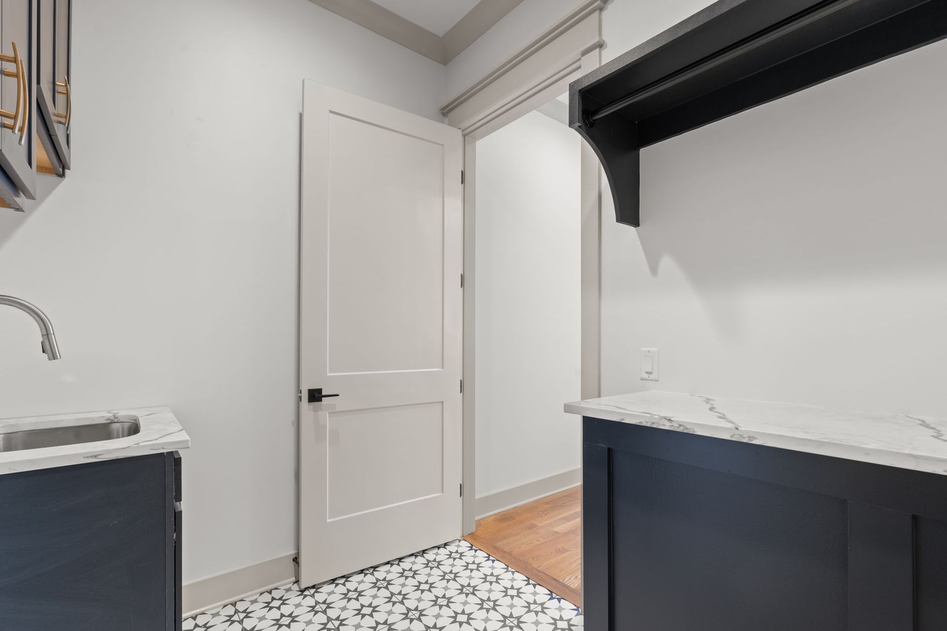Small laundry room with white door, black cabinets, patterned tile floor, and a sink counter