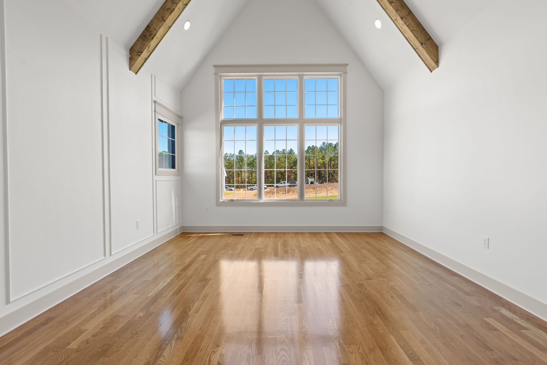 Empty attic-style room with hardwood floors, white walls, and a large window at the far end.
