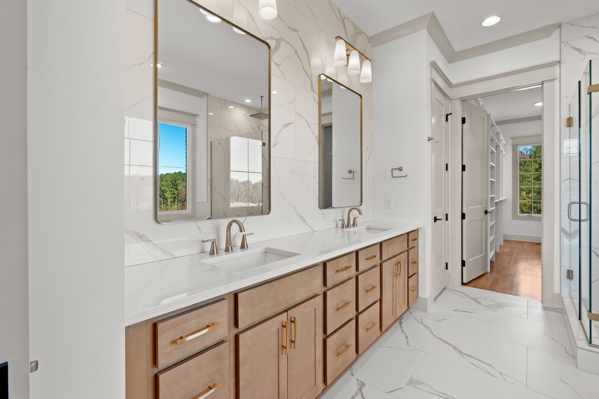 Bright modern bathroom with double vanity, marble counters, wood cabinets, and large mirrors.