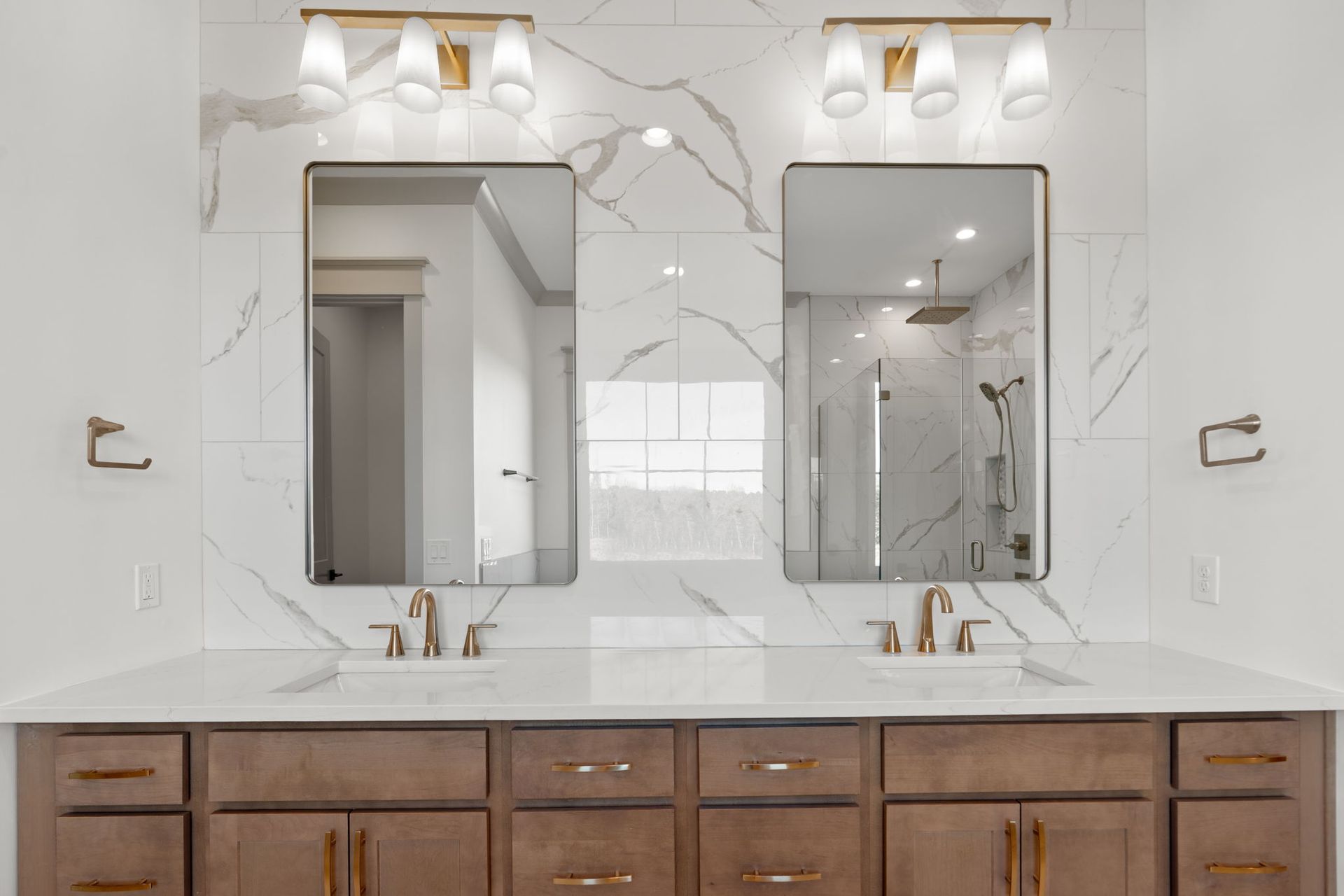 Modern bathroom vanity with double mirrors, white marble backsplash, and wood cabinets