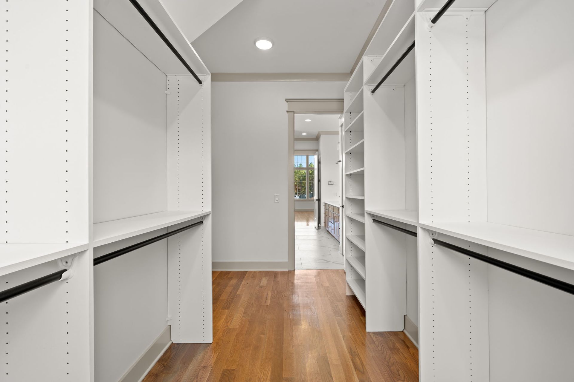 Bright walk-in closet with white shelves and wood floor leading to a doorway.