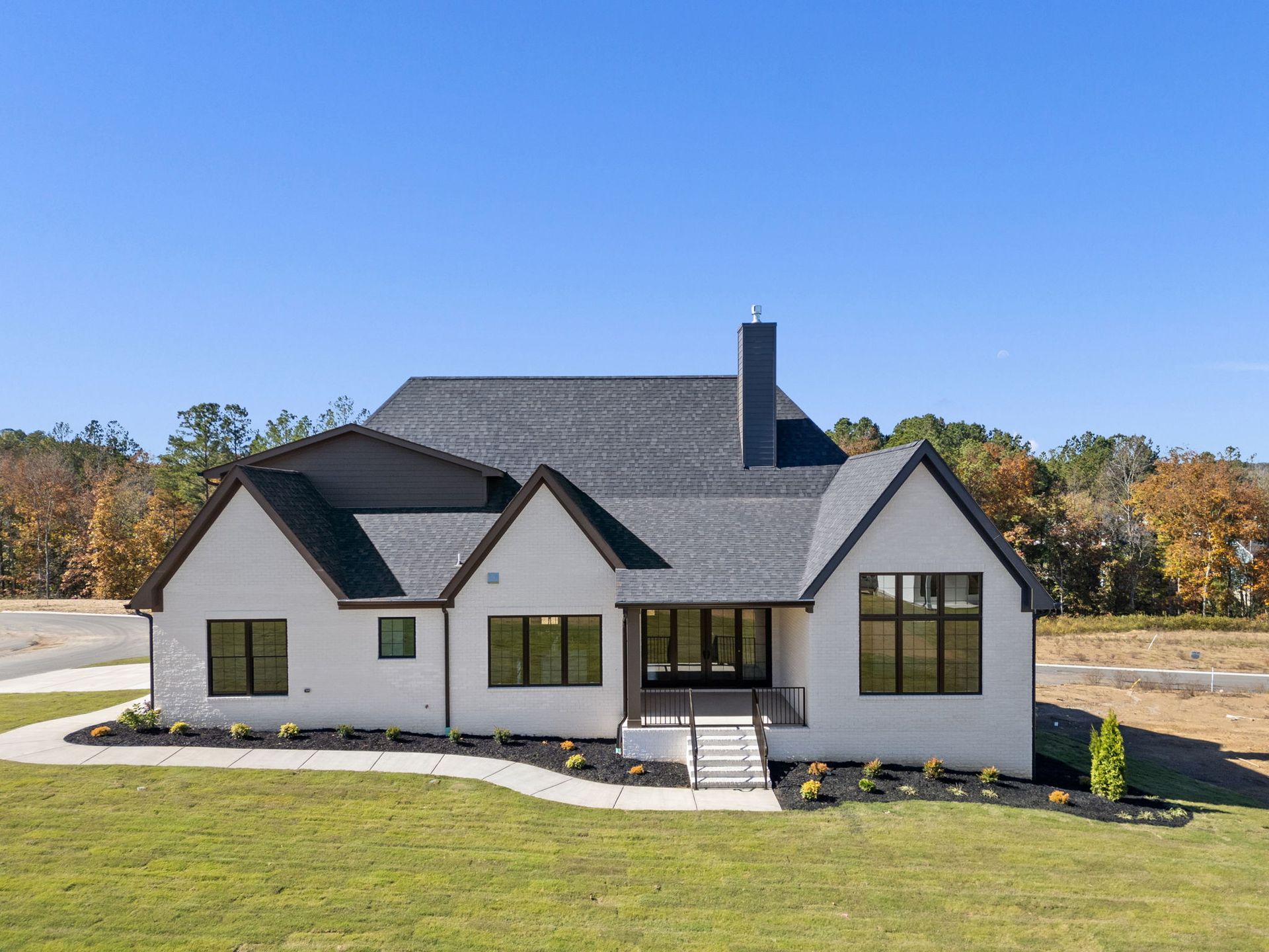 Modern white house with dark roof and front porch on a grassy lot under a clear blue sky