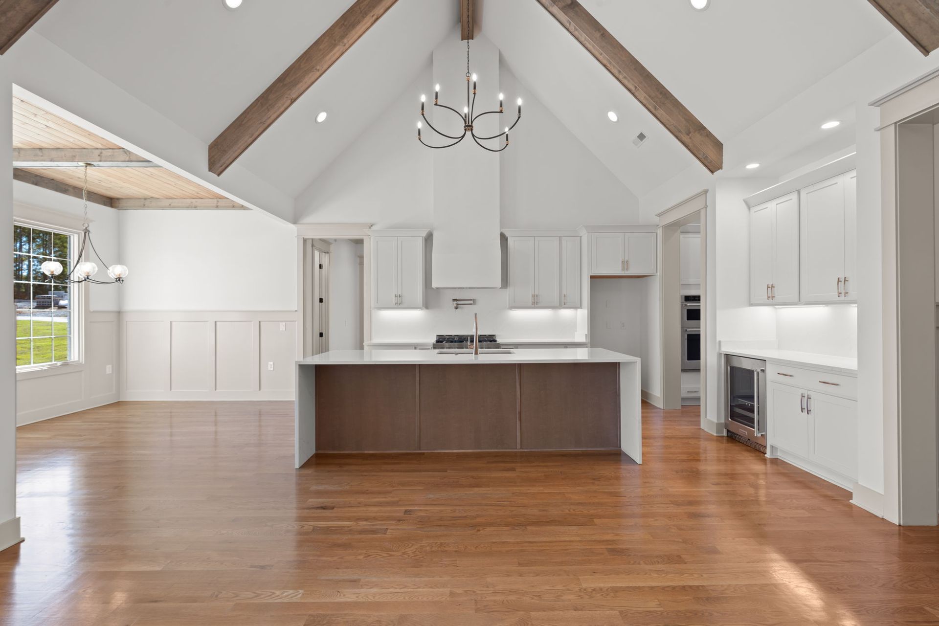 Bright open kitchen with white cabinets, large island, hardwood floors, and vaulted ceiling with exposed beams.