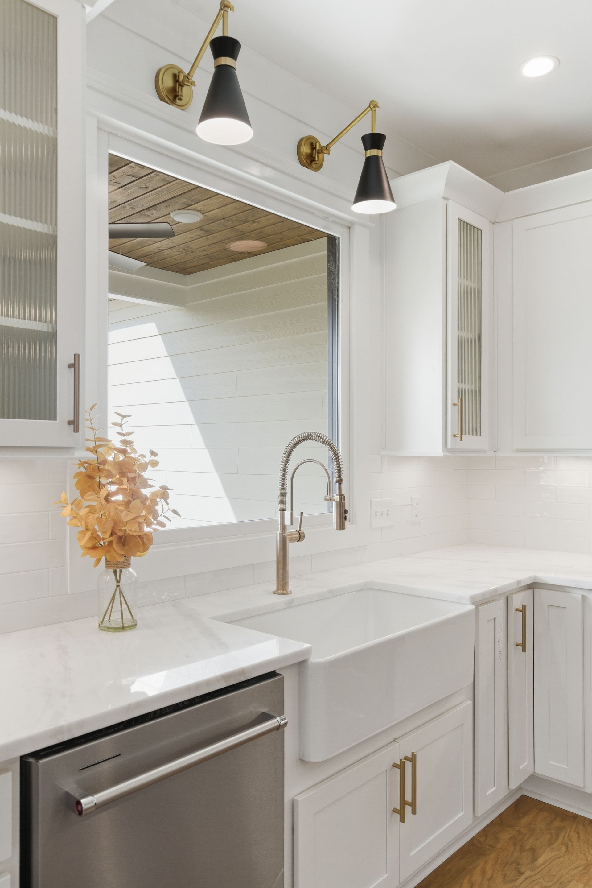 Bright white kitchen with marble sink, gold fixtures, black-and-gold lights, and a decorative vase on the counter