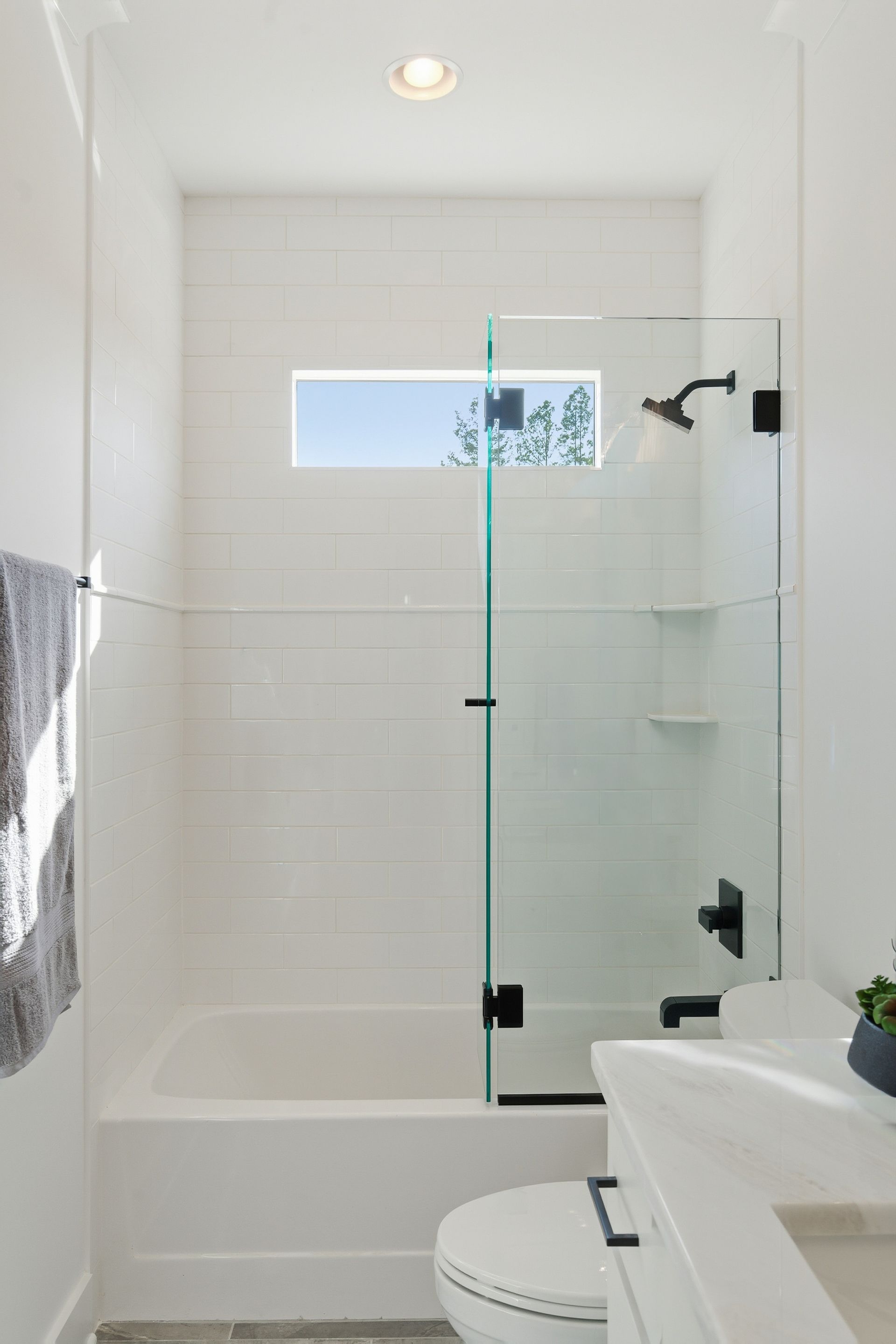 Modern white bathroom with a walk-in shower, glass door, and toilet in the foreground