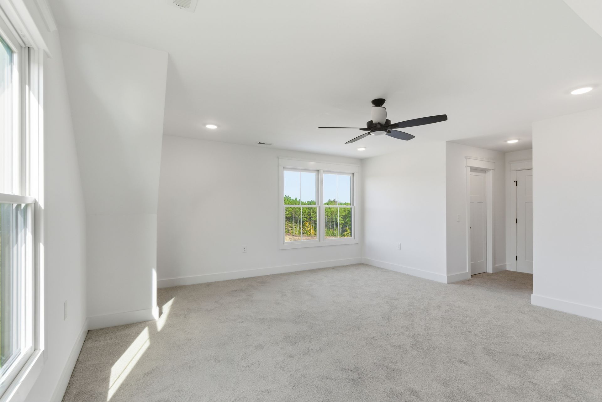 Bright empty bedroom with gray carpet, white walls, ceiling fan, and two windows.