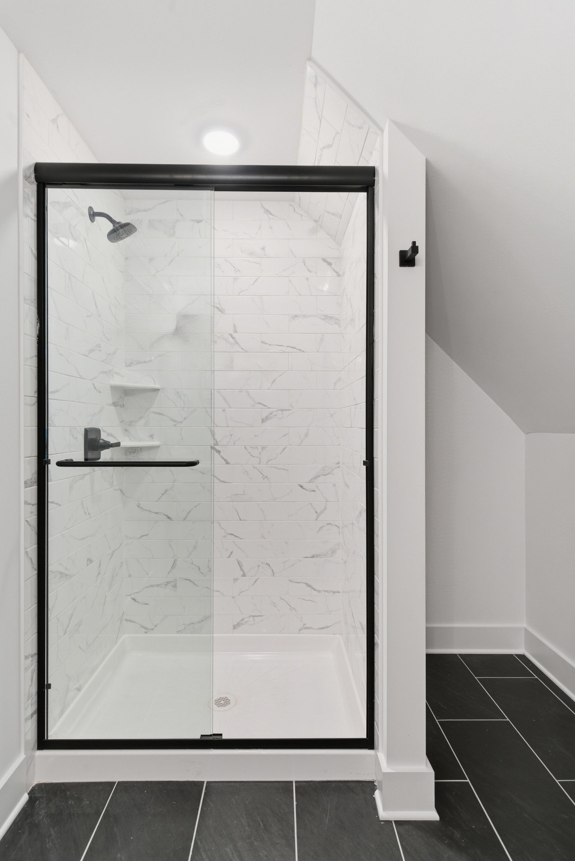 Black-framed glass shower enclosure in a modern white-tiled bathroom.