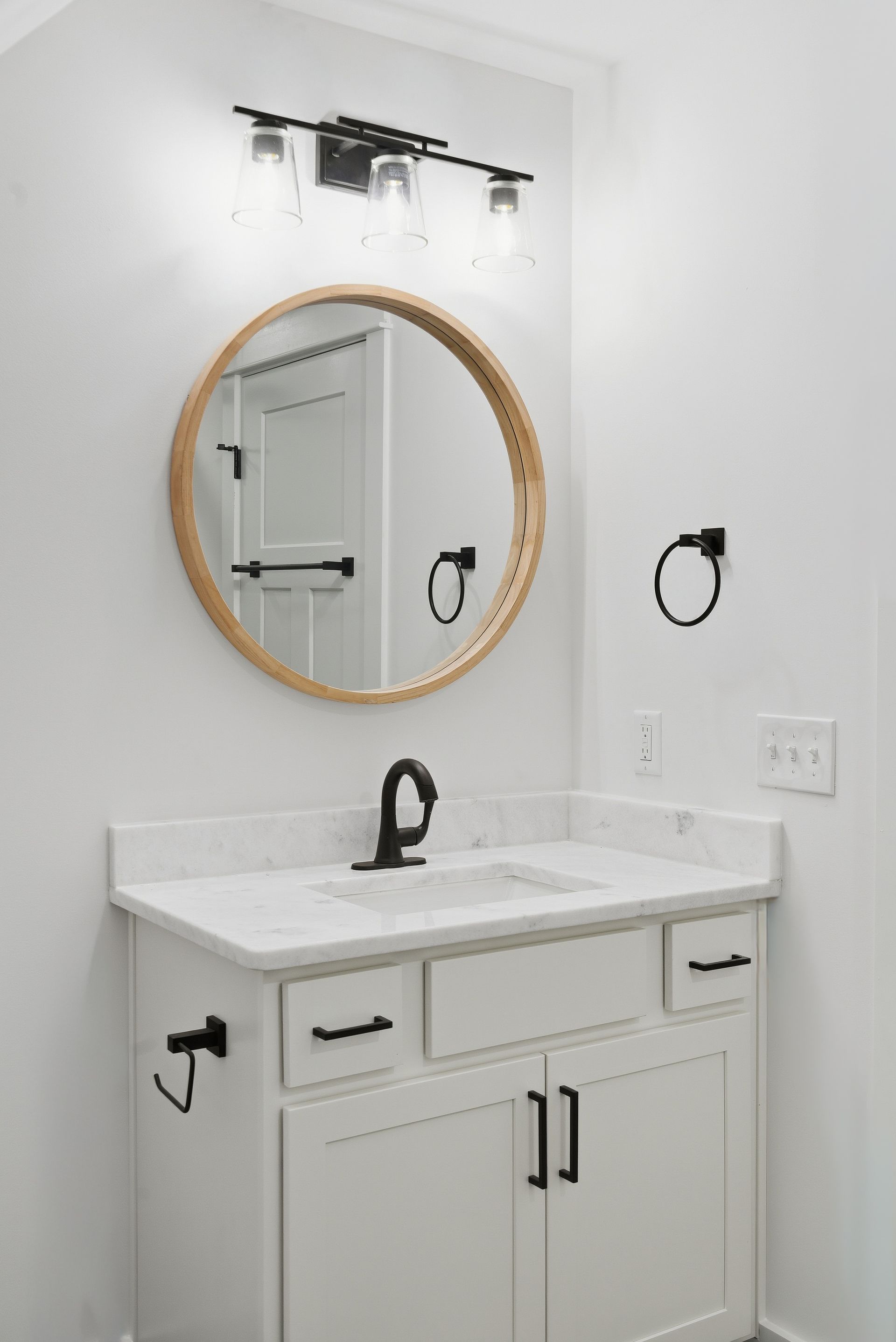 Modern white bathroom vanity with round wood-framed mirror and black fixtures
