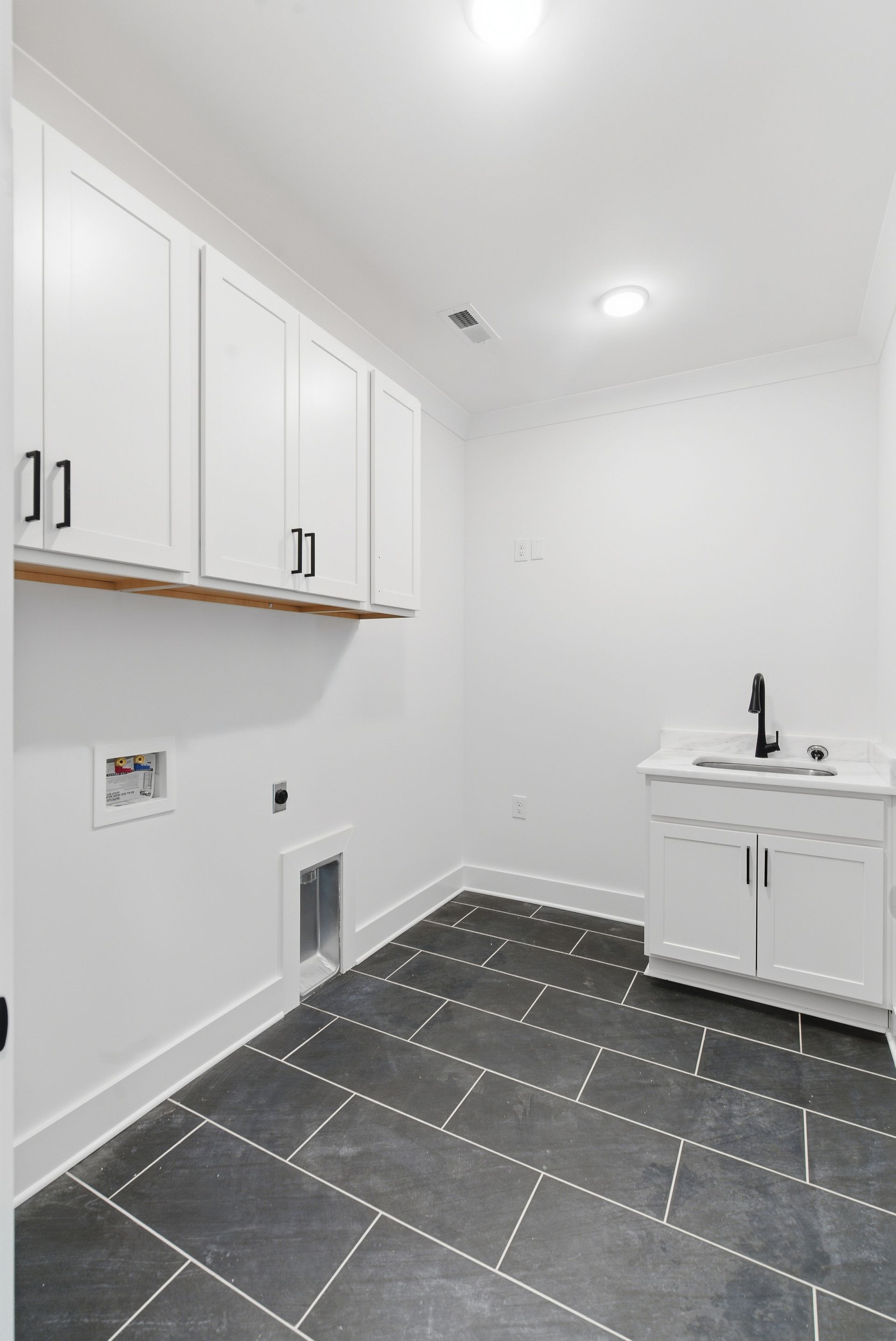 White laundry room with cabinets, sink, and dark tiled floor