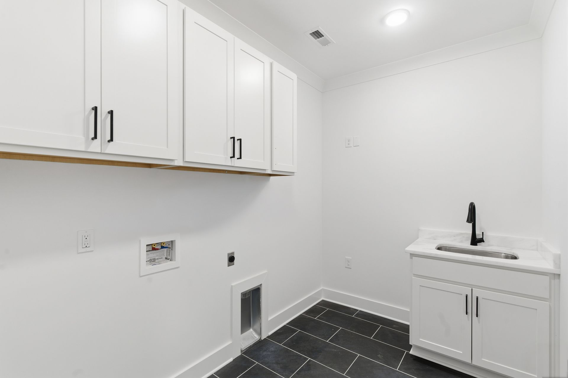 Bright laundry room with white cabinets, black tile floor, and utility sink