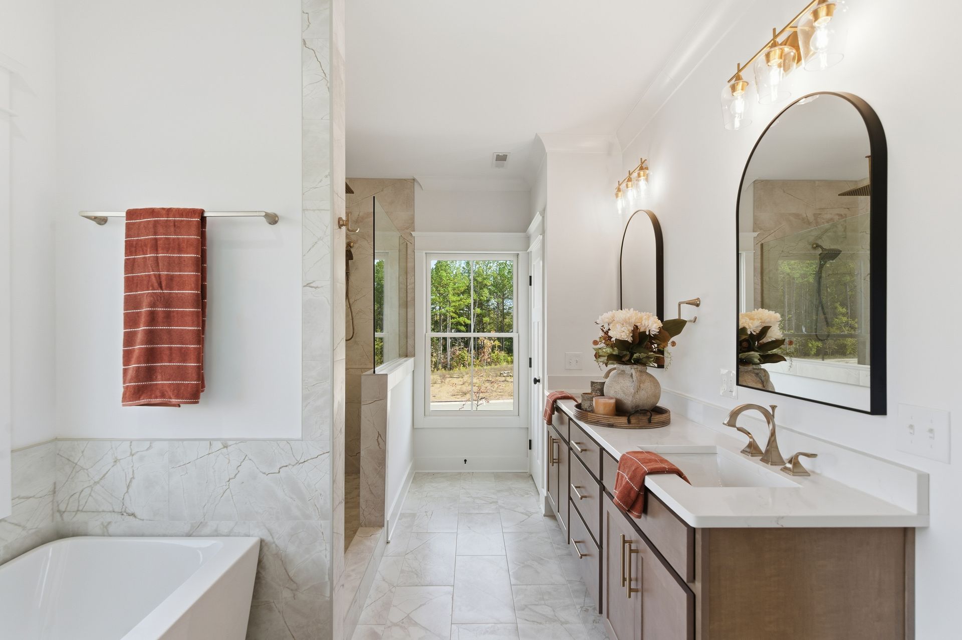 Bright white bathroom with marble accents, double vanity, arched mirrors, and a towel by the tub