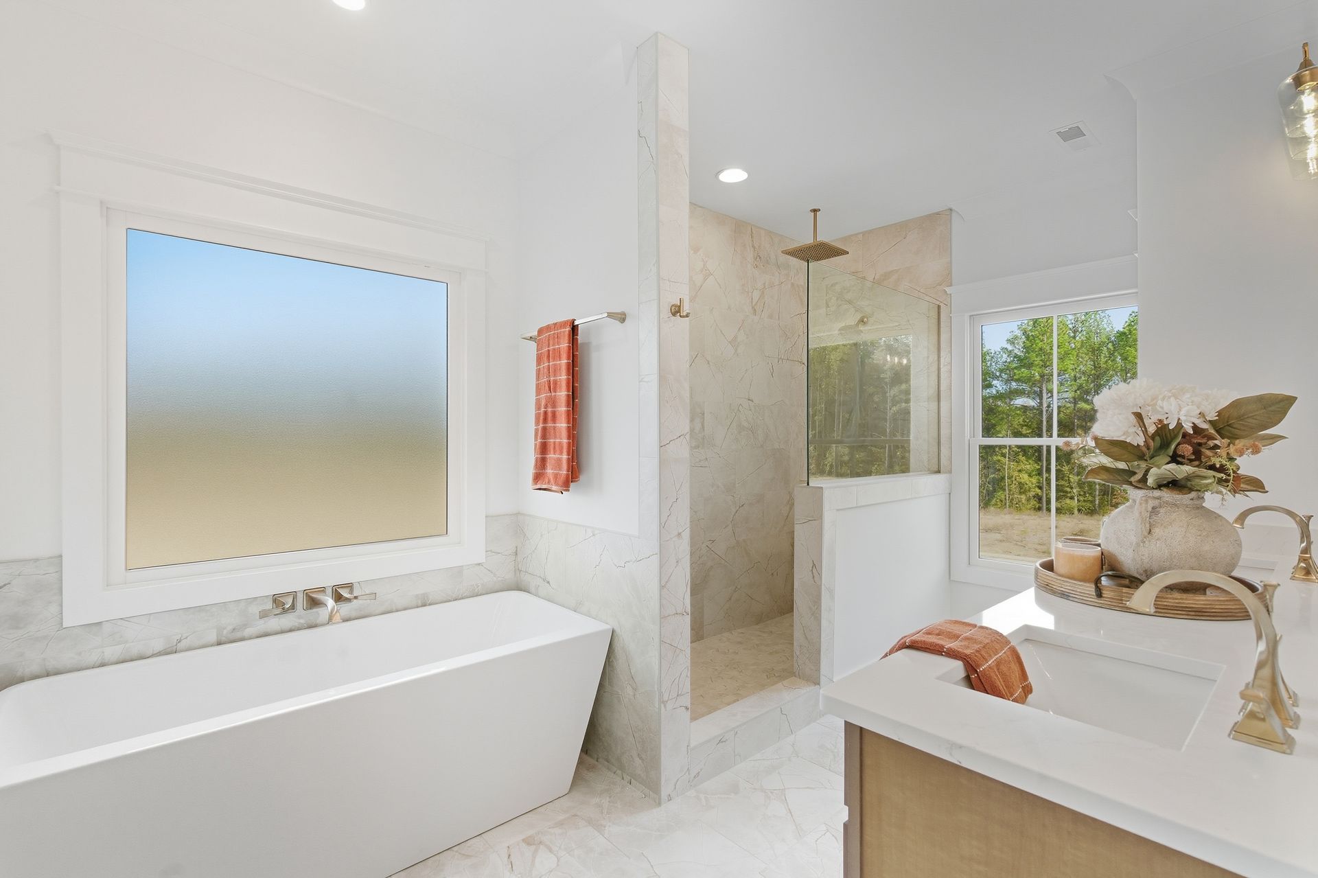 Bright white bathroom with freestanding tub, glass shower, double vanity, and large frosted window.