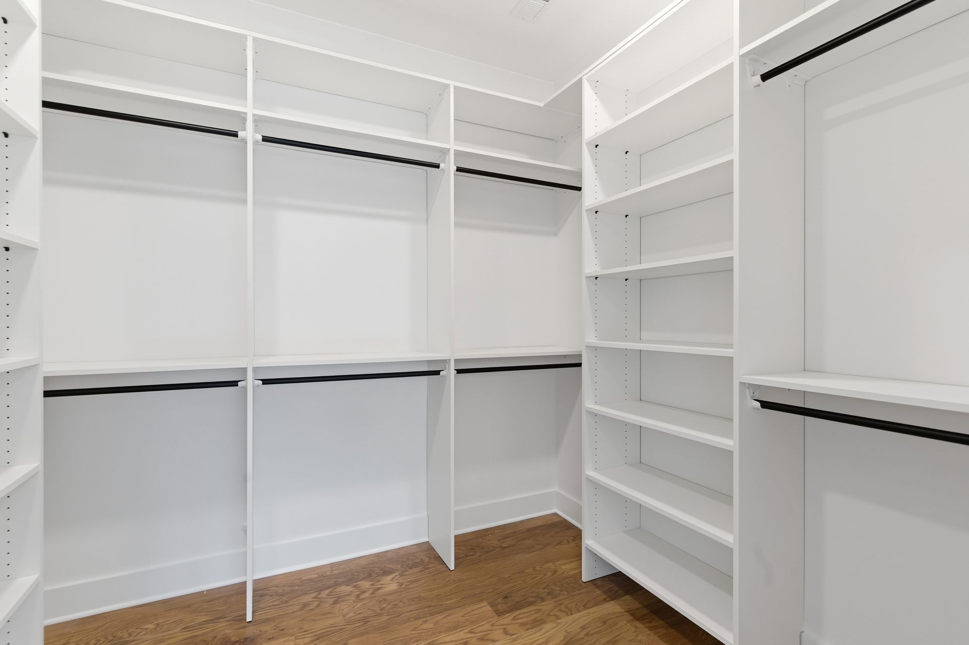 Empty white walk-in closet with built-in shelves, hanging rods, and wood floor