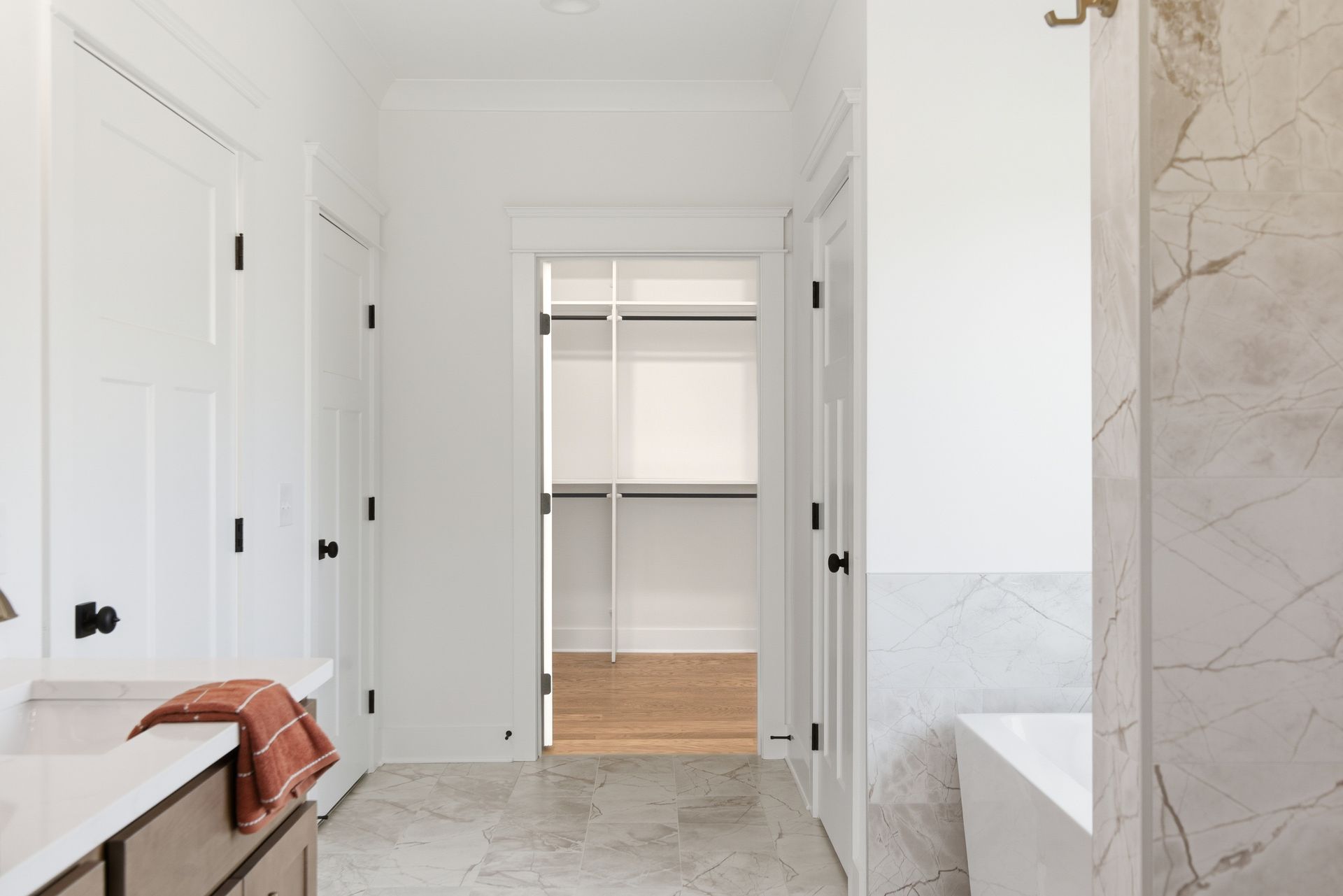 Bright hallway with white doors, marble tile floor, and an open closet ahead.
