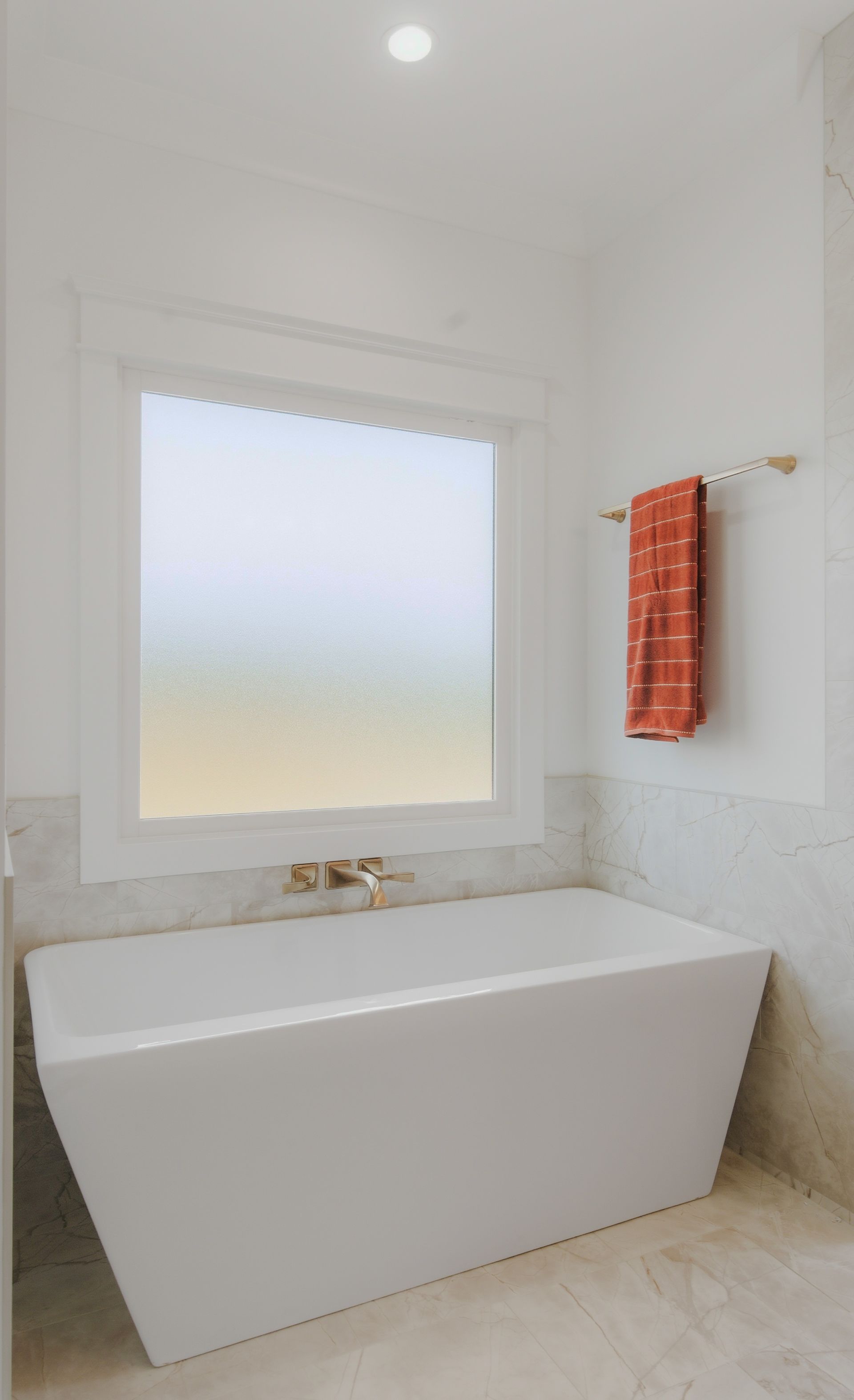 Modern white bathroom with a freestanding tub, window, and orange towel rack.
