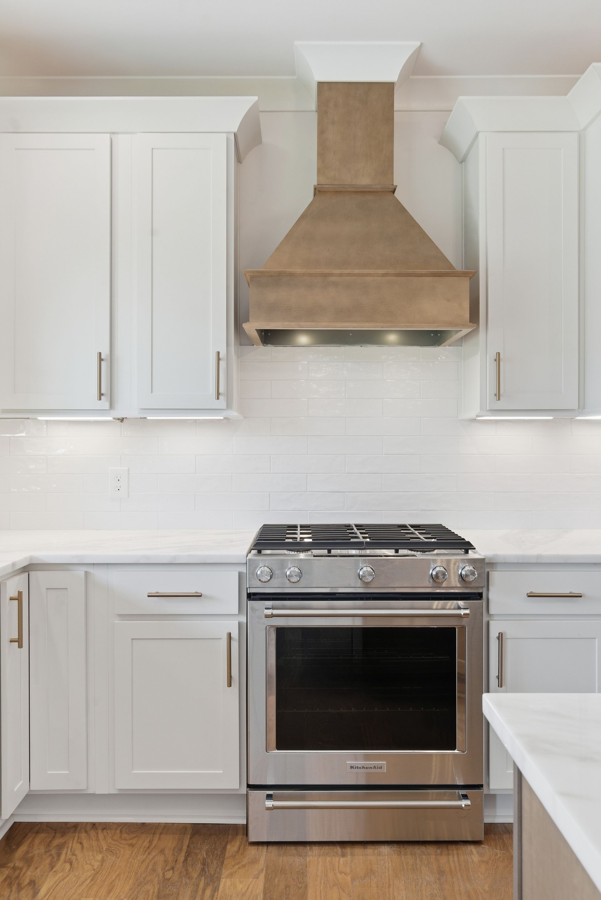 Modern kitchen with white cabinets, stainless steel stove, and beige range hood