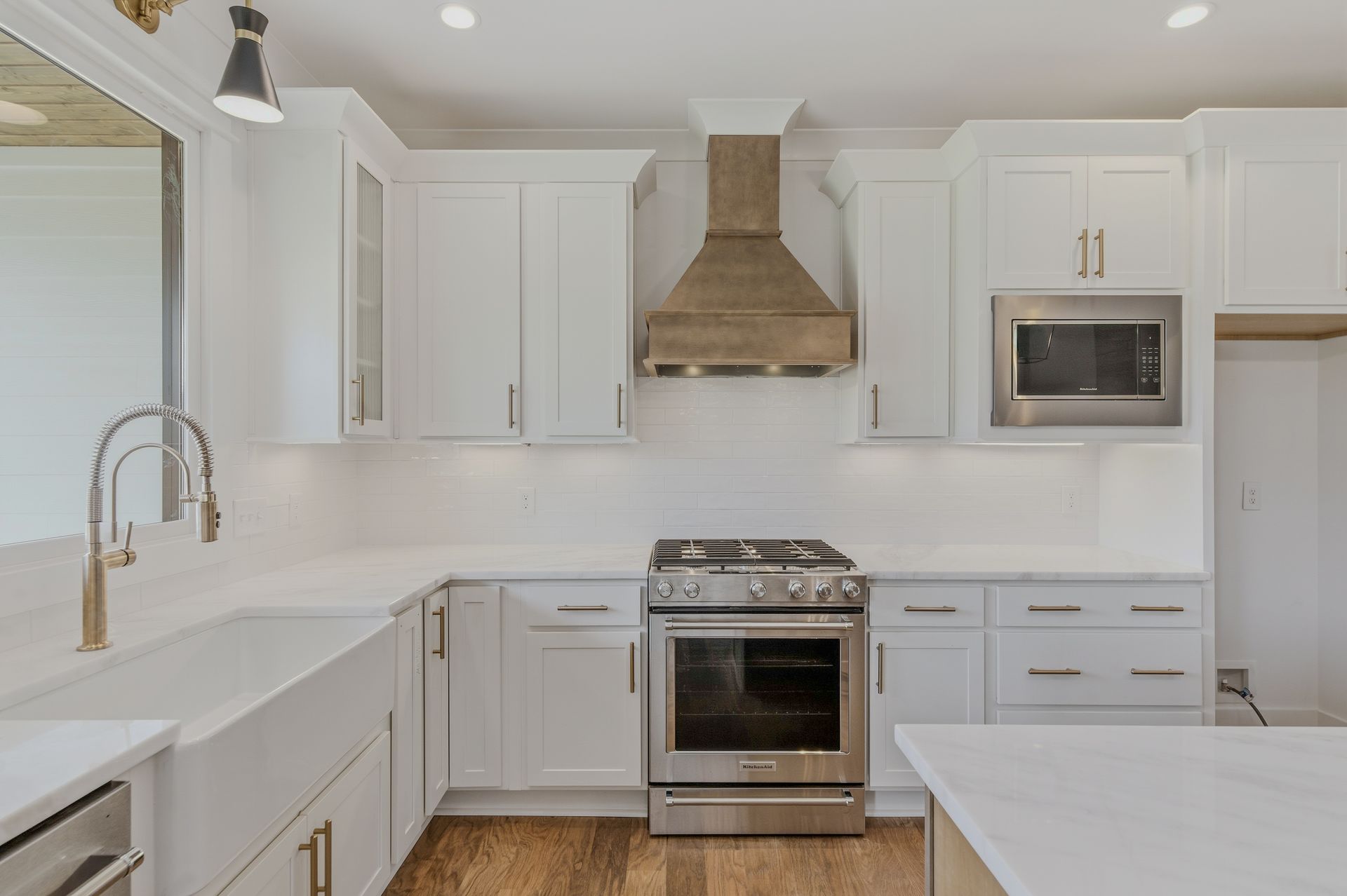 Bright white modern kitchen with stainless steel stove, hood, microwave, and large sink.