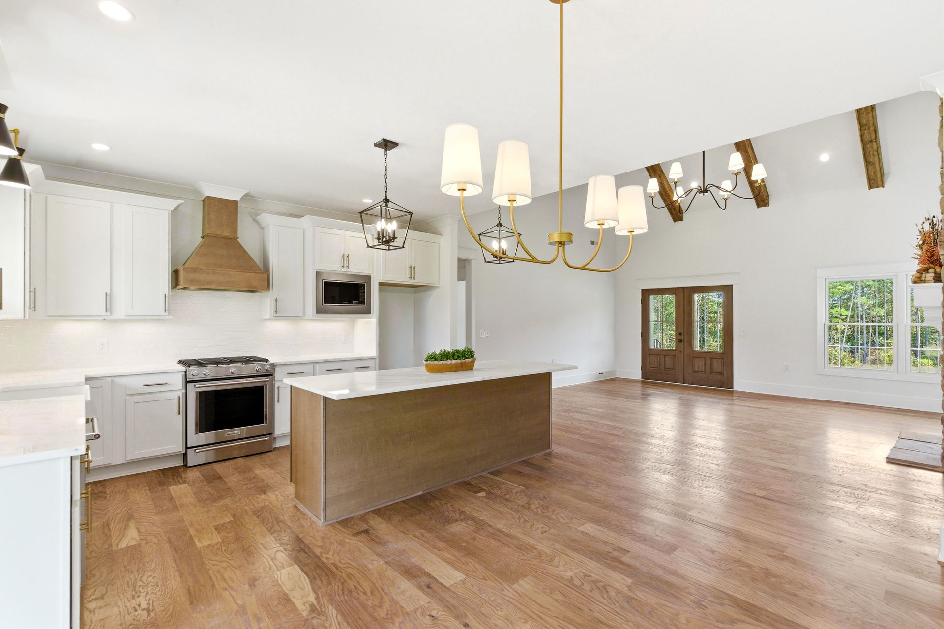 Bright open kitchen and dining area with white cabinets, wood floors, island, and chandeliers
