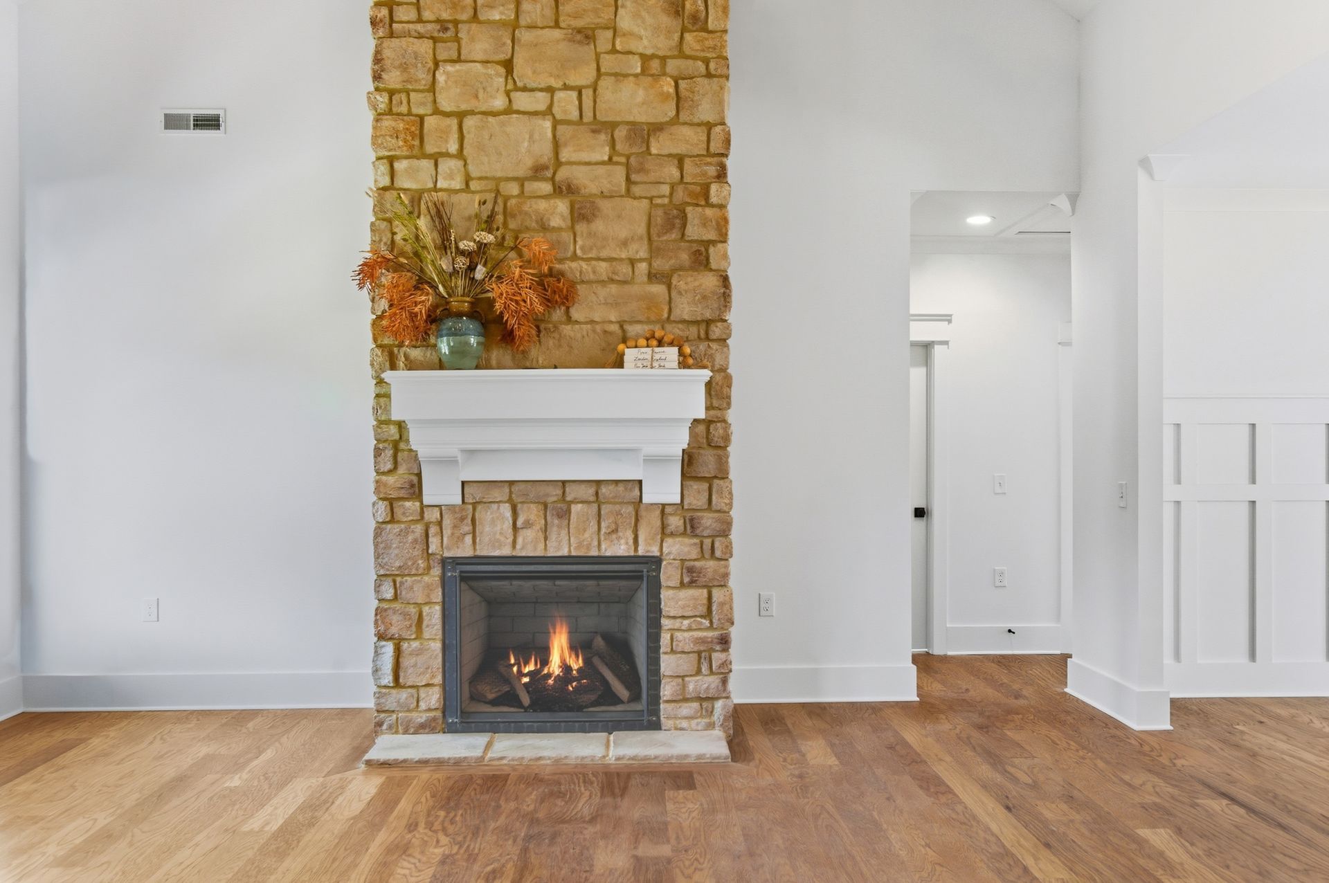 Living room with stone fireplace, white mantel, hardwood floors, and open doorway