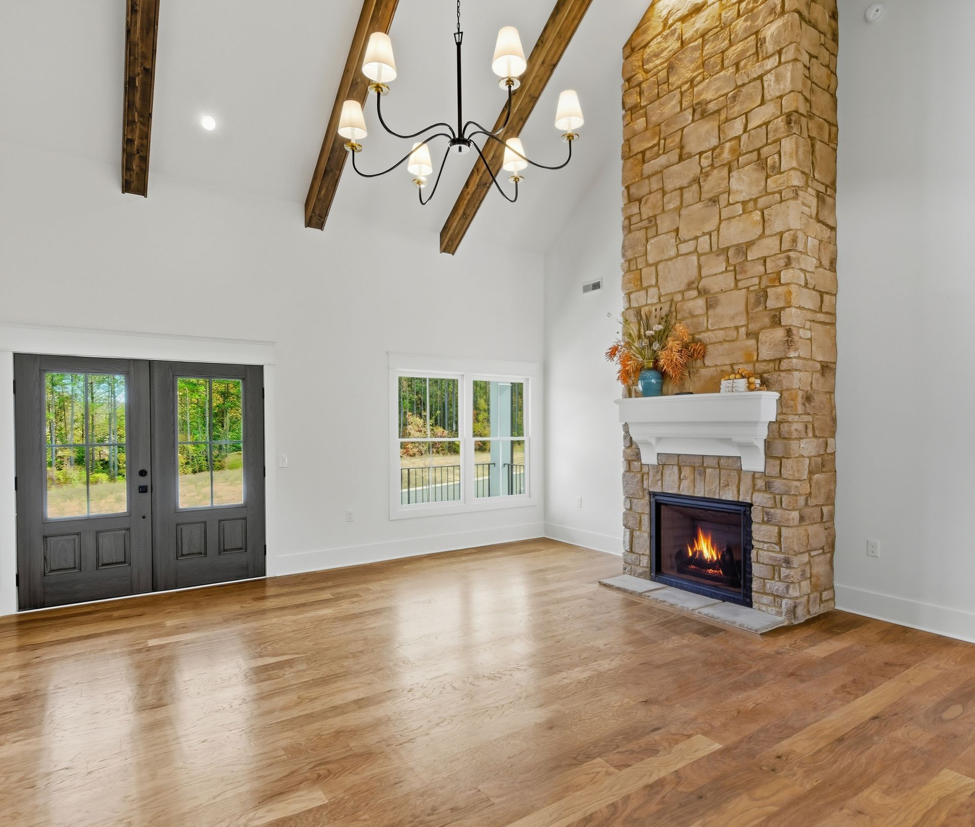 Spacious living room with stone fireplace, vaulted ceiling, wood beams, and dark double doors