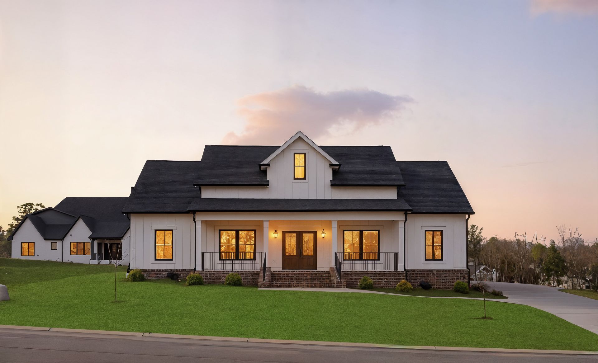 Modern white farmhouse-style house with lit windows at dusk and a green lawn in front
