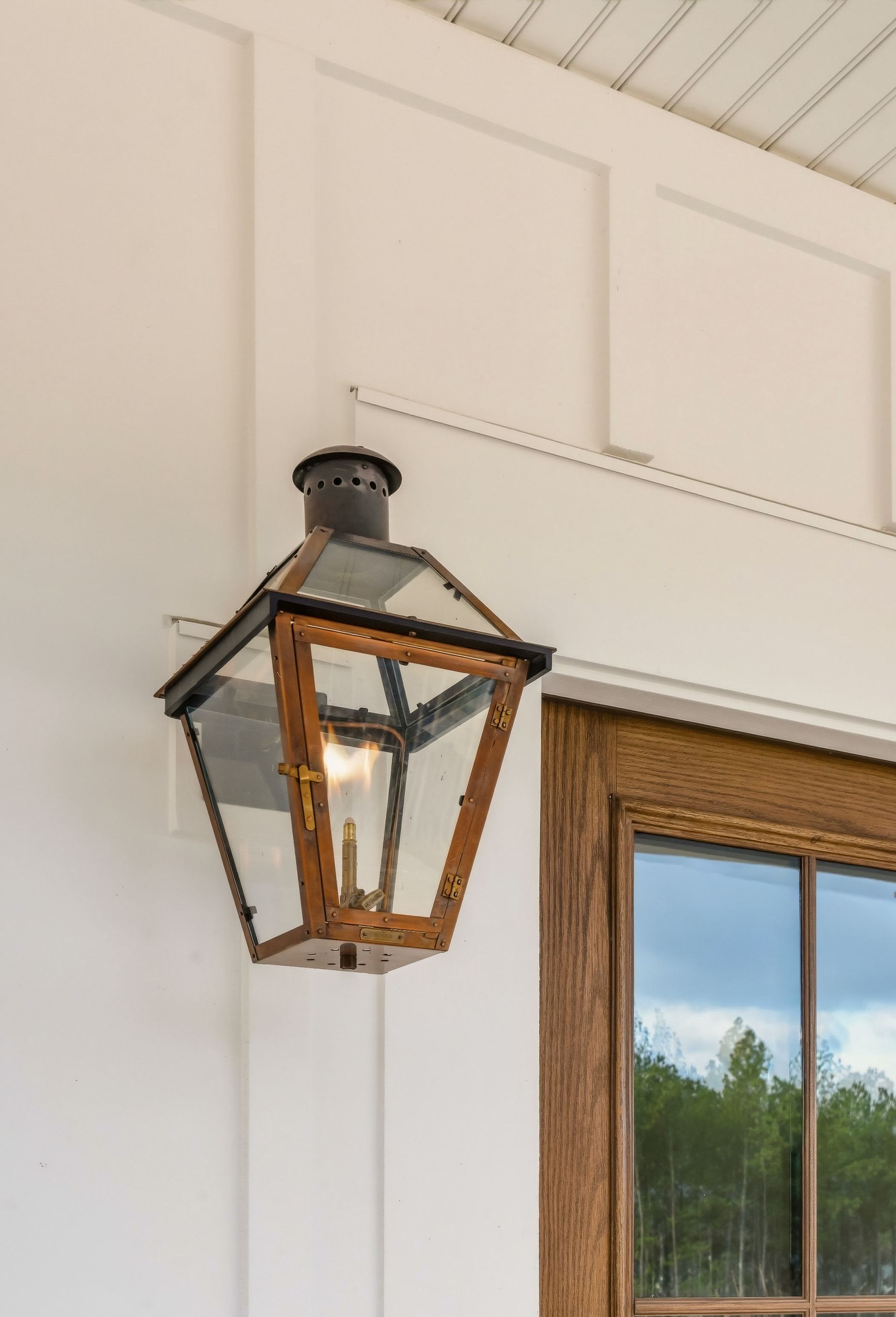 Black metal lantern-style wall sconce beside a window on a white exterior wall
