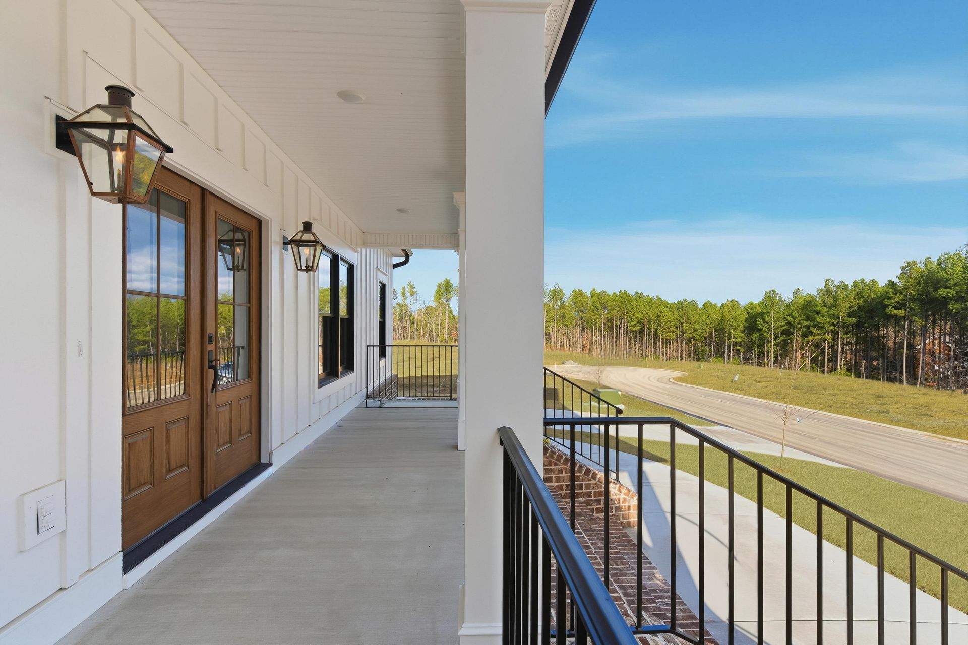Covered porch with white columns, black railings, and double wooden doors overlooking a grassy landscape.