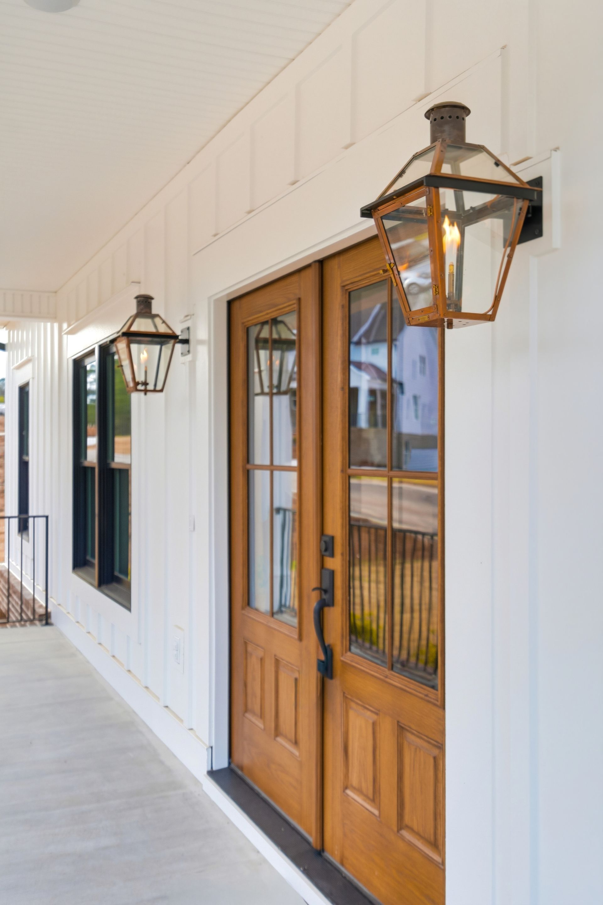 White storefront walkway with wooden double doors and black lantern-style wall lights