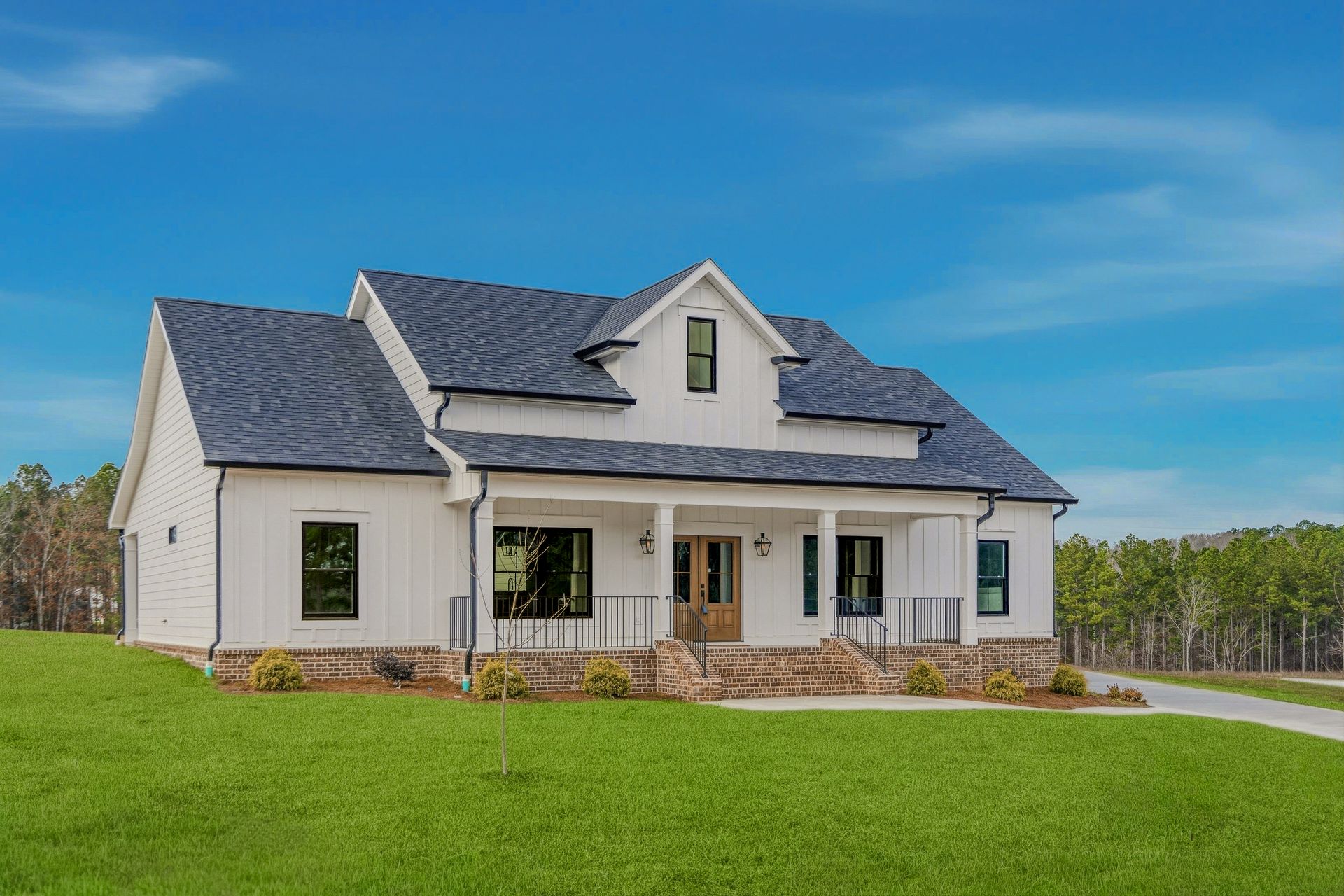 White farmhouse with dark roof and porch on a green lawn under a blue sky