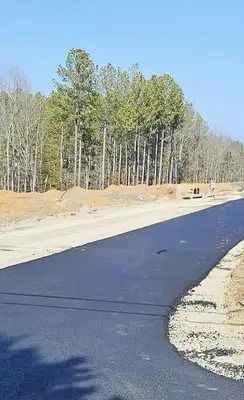 Fresh black asphalt road curving through a sandy, wooded construction area on a clear day