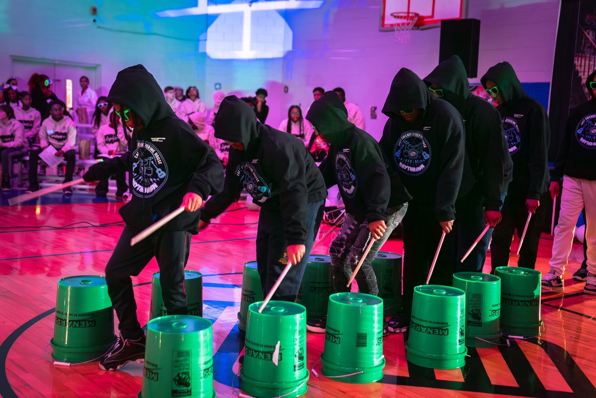 People in black hijabs play a bucket drum game in a colorful indoor gymnasium.