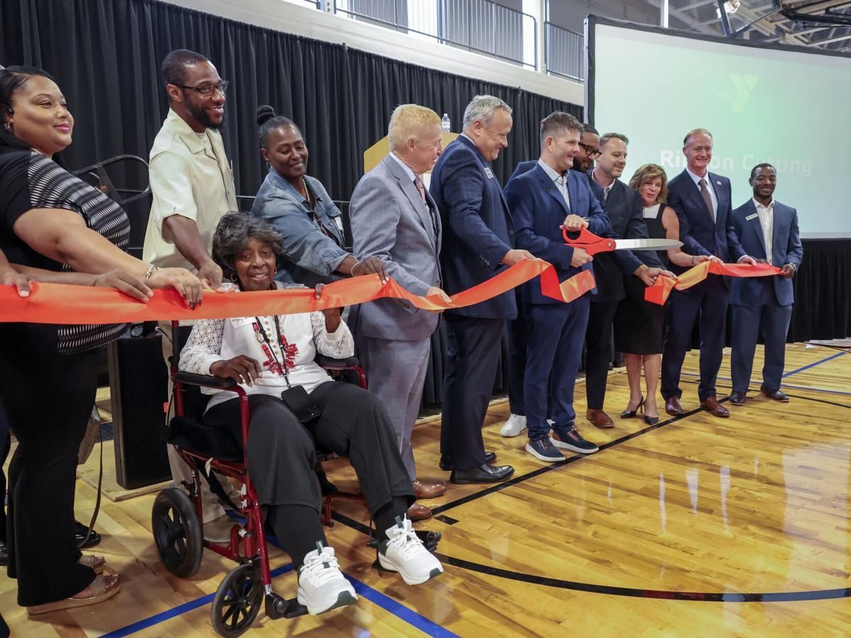 Ribbon-cutting ceremony on a gym floor, with officials and a seated child holding a red ribbon.