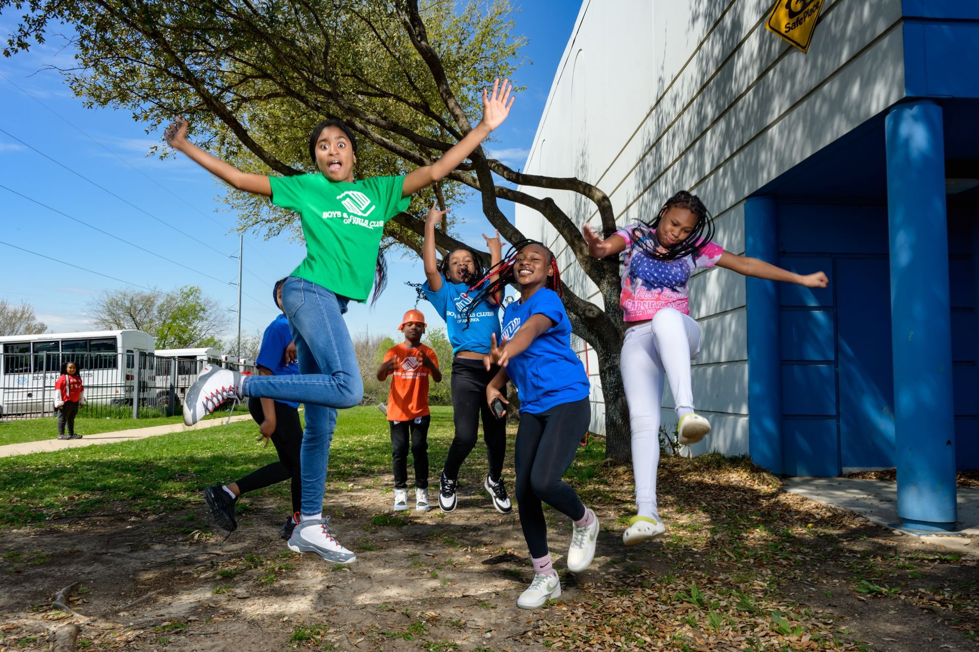 Children jumping and posing happily outside a blue building in bright daylight