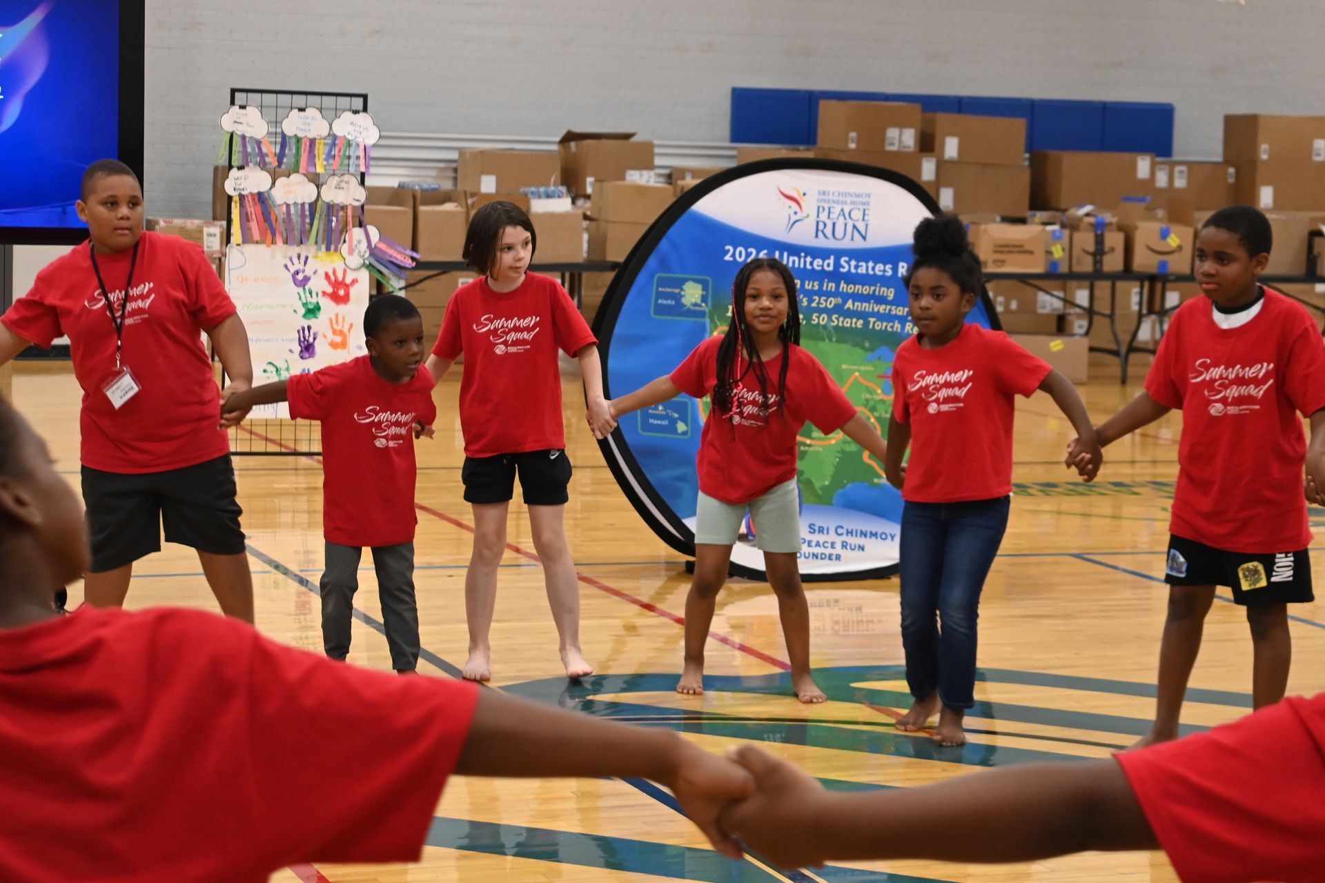 Children in red shirts holding hands in a gym during an indoor group activity