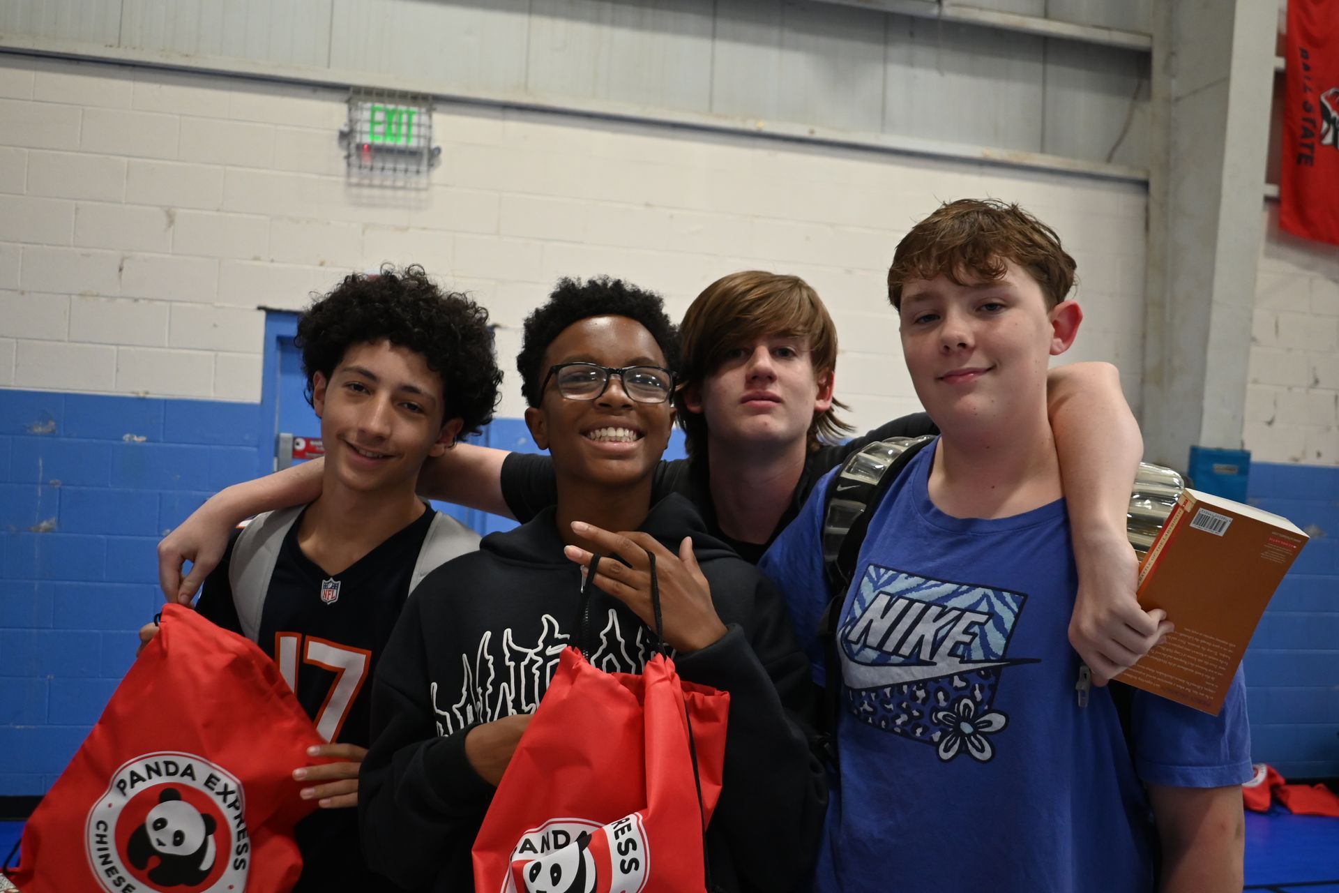 Four students pose indoors holding red award bags, smiling in a gymnasium.