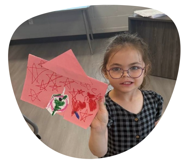 Smiling child holding a pink paper craft with red star doodles in a classroom