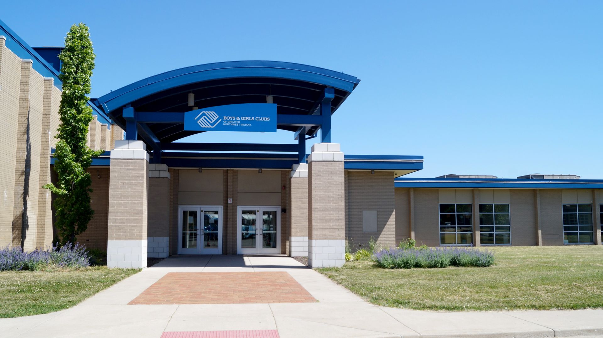 Front entrance of a modern brick building with a blue awning and glass doors.