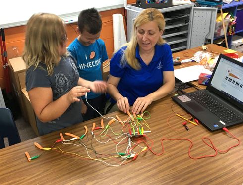 Three people working with colorful wires at a table beside a laptop in a classroom or lab